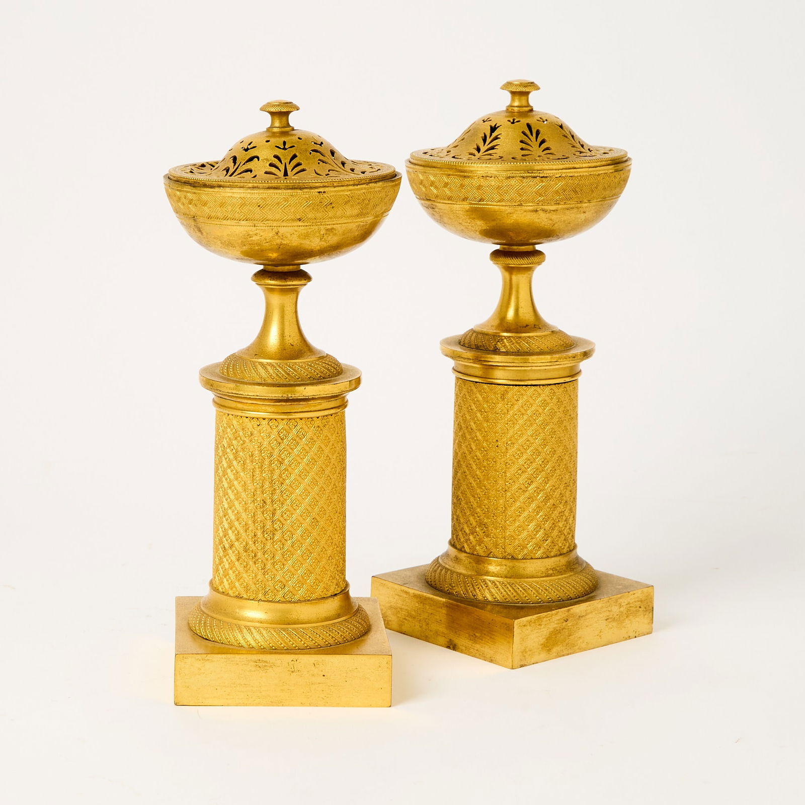 Pair of Empire Ormolu Cassolettes: Circa 1810 Each a double usage, the pierced covers reversible to reveal candlesticks, mounted on a square plinth supporting a cylindrical shaft, the upper section formed as a circular bowl with finely