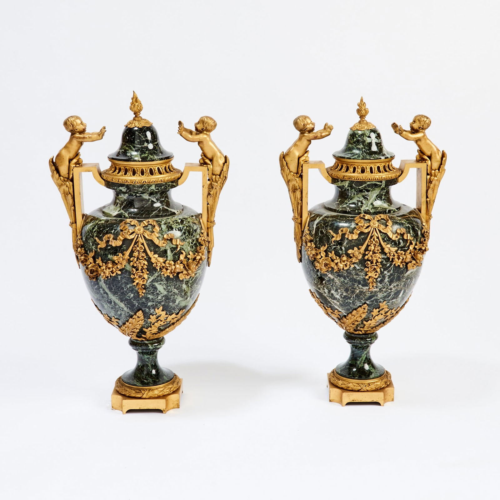 Pair of Louis XVI Style Gilt-Bronze Mounted Verde Antico Marble Urns and Covers: Late 19th century Each baluster urn is centered by a ribbon-tied bow and floral swags flanked by two putti and acanthus-form handles, on a flaring socle and ribbon-tied acanthus foot on a square plint