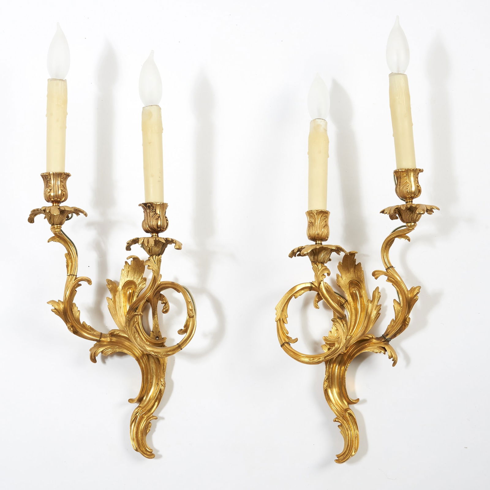 Pair of Louis XV Two-Branch Gilt-Bronze Wall Lights: Mid-18th century Each with shaped backplate issuing two scrolling candle arms finely cast with asymmetrical C-scrolls and acanthus leaves, fitted with foliate drip pans and urn-form nozzles. Height 13