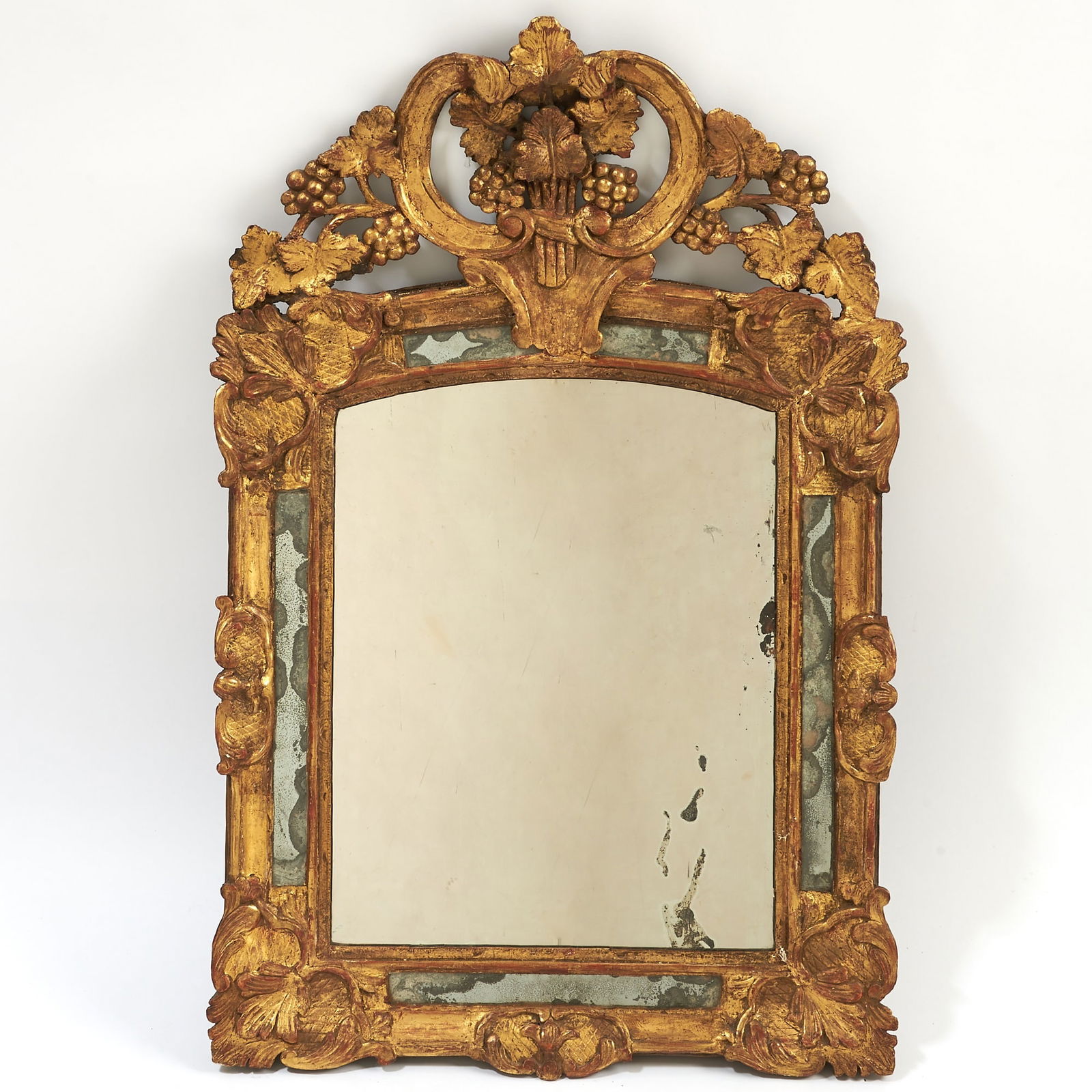 Louis XVI Provincial Carved Giltwood Mirror: The Property of a Distinguished Private Collection Last quarter 18th century The rectangular plate within a moulded frame carved with scrolling foliage and rocailles, surmounted by an elaborate arched
