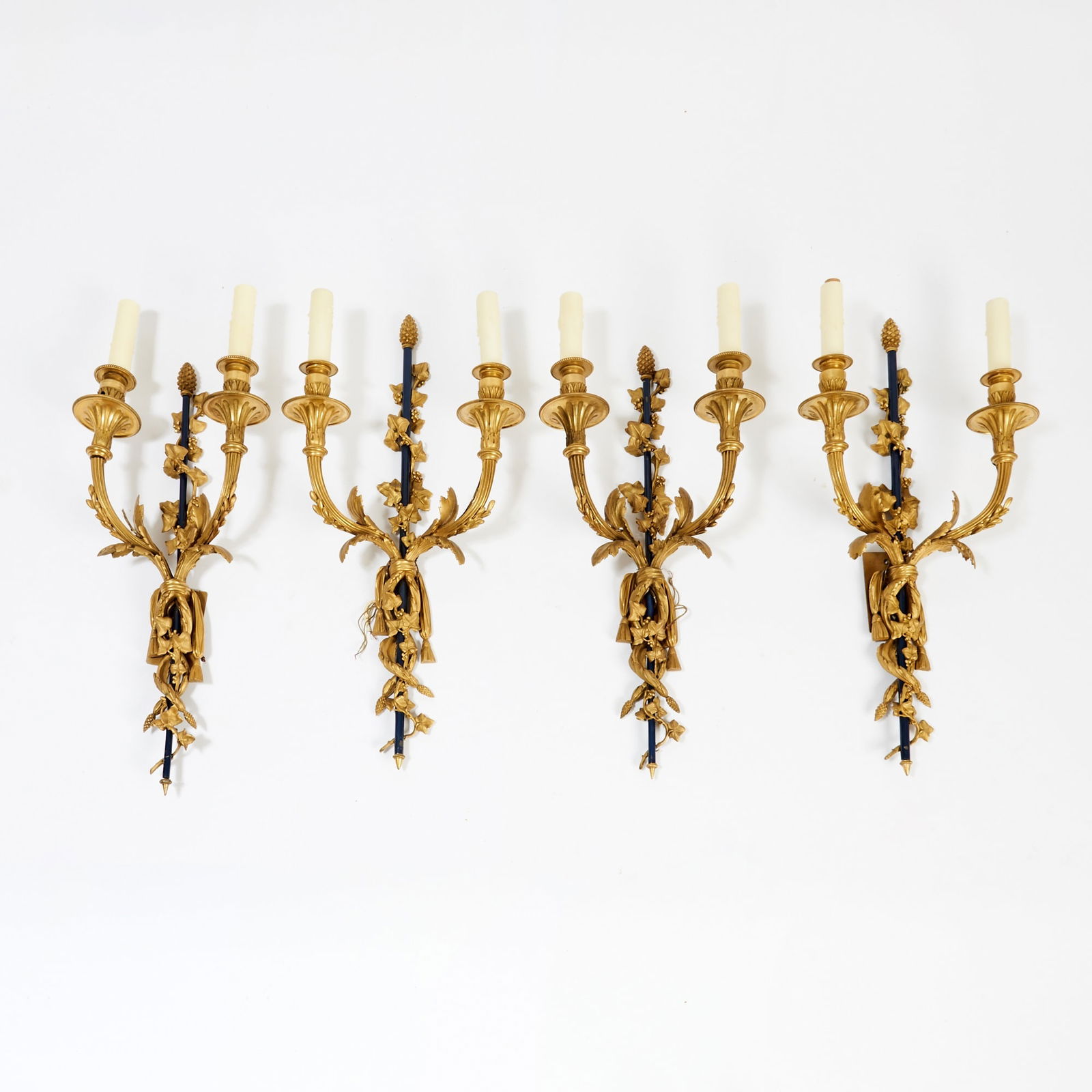 Set of Four Louis XVI Style Gilt and Patinated Bronze Two-Branch Wall Lights: Late 19th century Each with a vertical upright backplate centred by a fluted shaft surnounted by a pinecone finial, issuing two scrolling candle arms