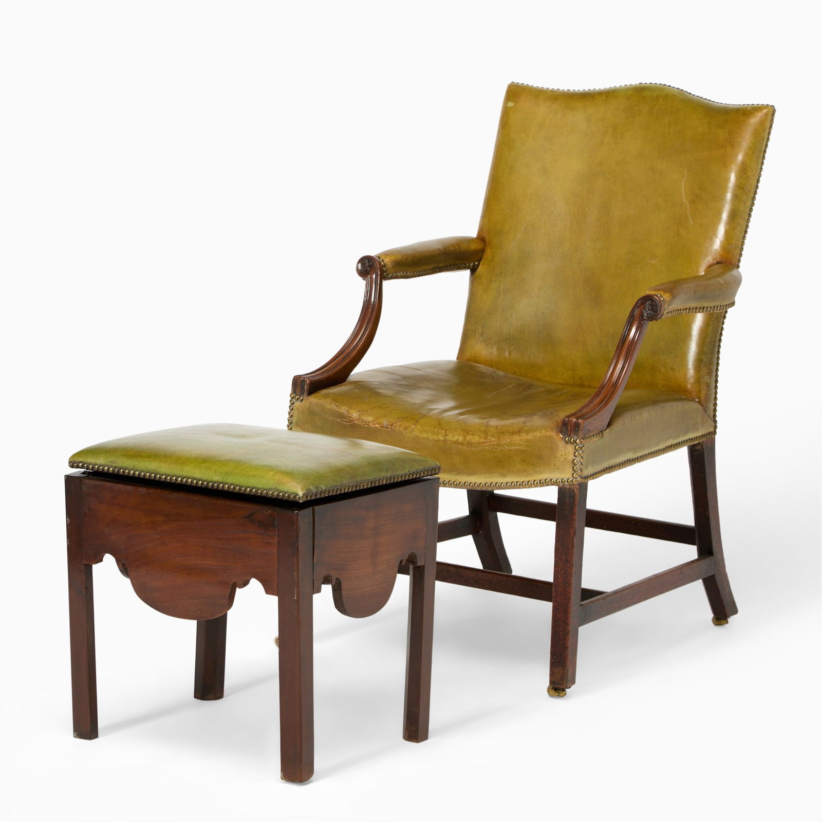George III Green Leather Mahogany Library chair Together with an Ottoman: Circa 1765 The serpentine padded back, arms, and seat flanked by downswept supports on chamfer legs joined by a stretcher and brass casters; Together with an ottoman. Chair 38 1/2 inches (97.7 cm), wi