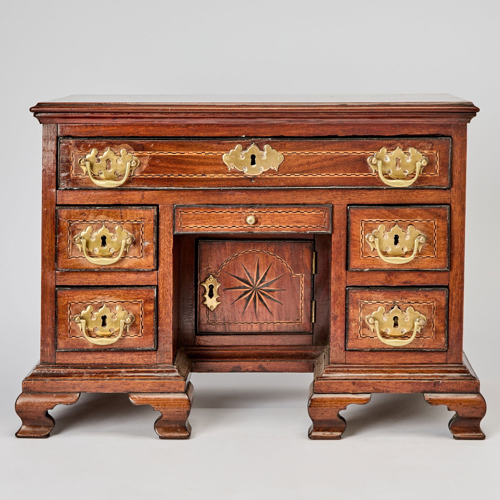 George III Style Diminutive Fruitwood Parquetry Inlaid Mahogany Kneehole Desk: 19th century The molded rectangular top above one long drawer over two banks of short drawers, the center with a secret drawer over a panel door enclosing shelves, on bracket feet. Height 14 1/2 inche