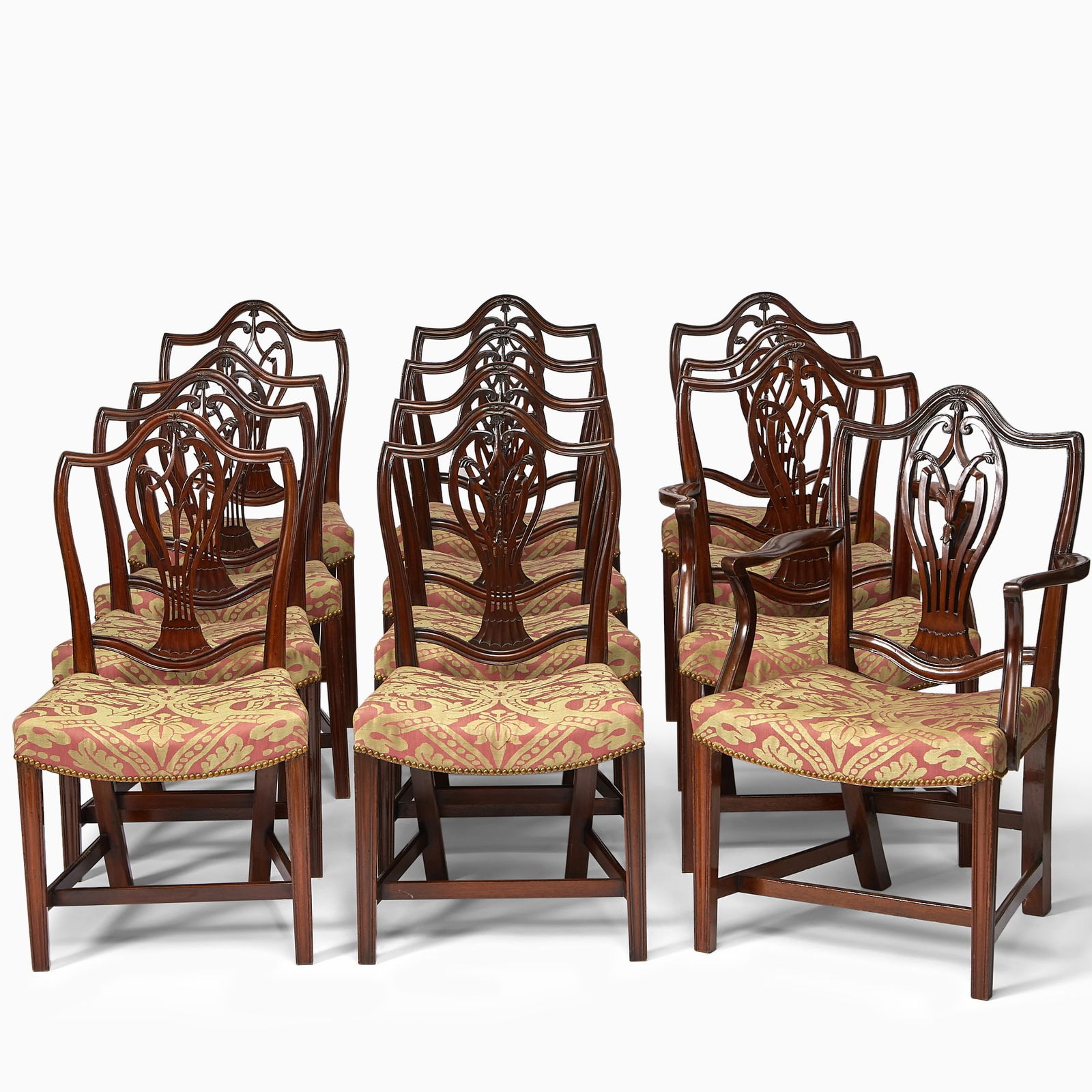 Assembled Set of Twelve George III Mahogany Armchairs: Circa 1785 and later Comprising two armchairs and eight side chairs, each with a shield back above a curvilinear pierced splat and shaped arms over down-swept supports, the curved seats covered in red