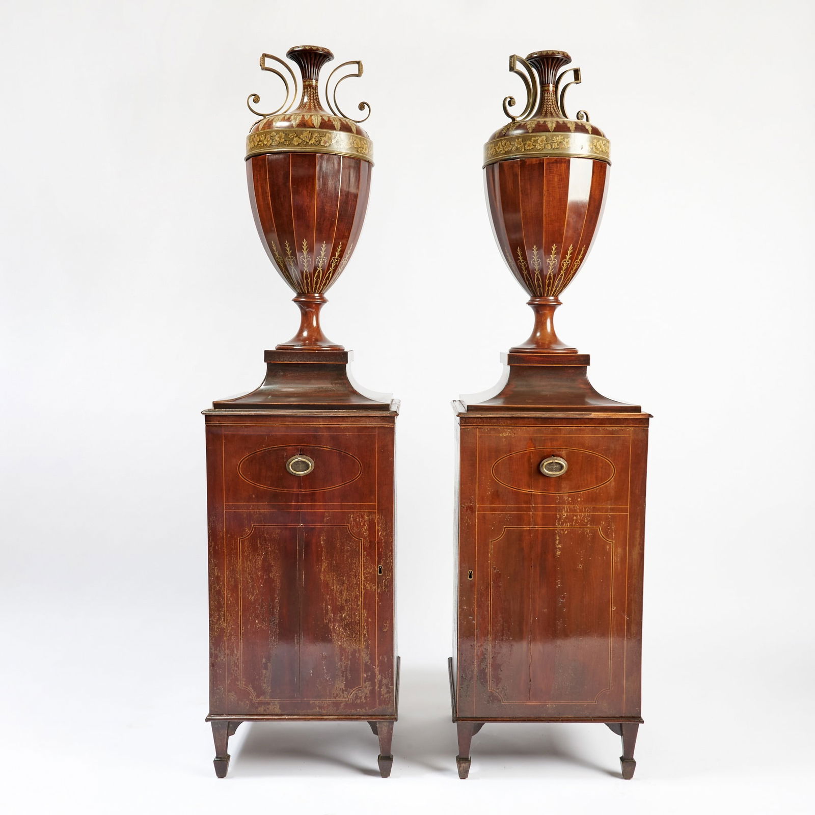 Pair of George III Mahogany and Painted Cutlery Urns on Stands: Each of round tapering form with telescope tops revealing a stepped fitted interior, on a turned socle above a fitted cabinet on splay legs. Height 73 inches (185.4 cm), width 18 1/2 inches (46.9 cm).