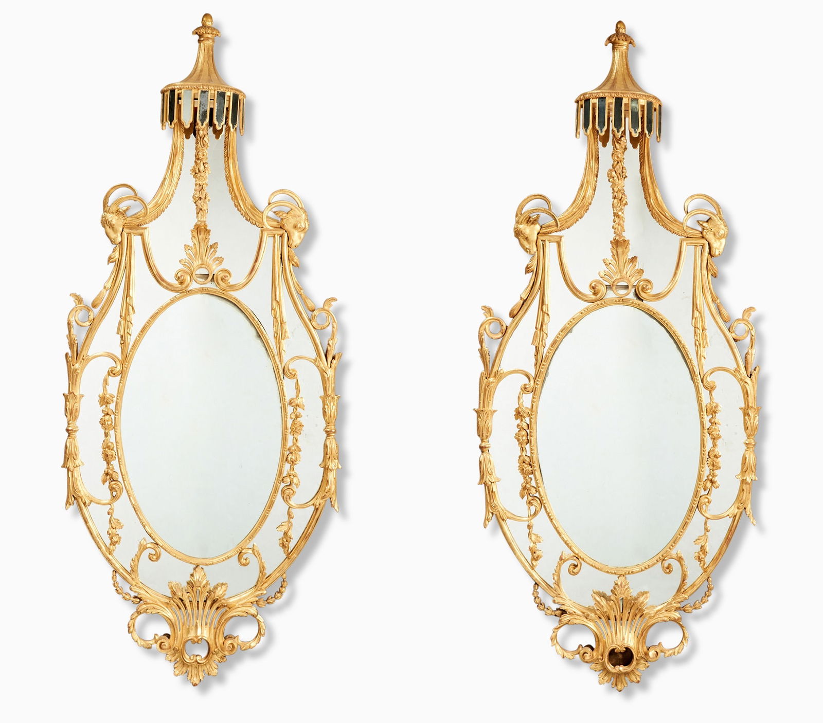 Pair of George III Giltwood Mirrors: Each oval central mirror plate surrounded by foliate and C-scroll-clasped mirror plates below a lambrequin cresting with trailing foliage and acanthus plume flanked by ram's heads, with pierced acanth