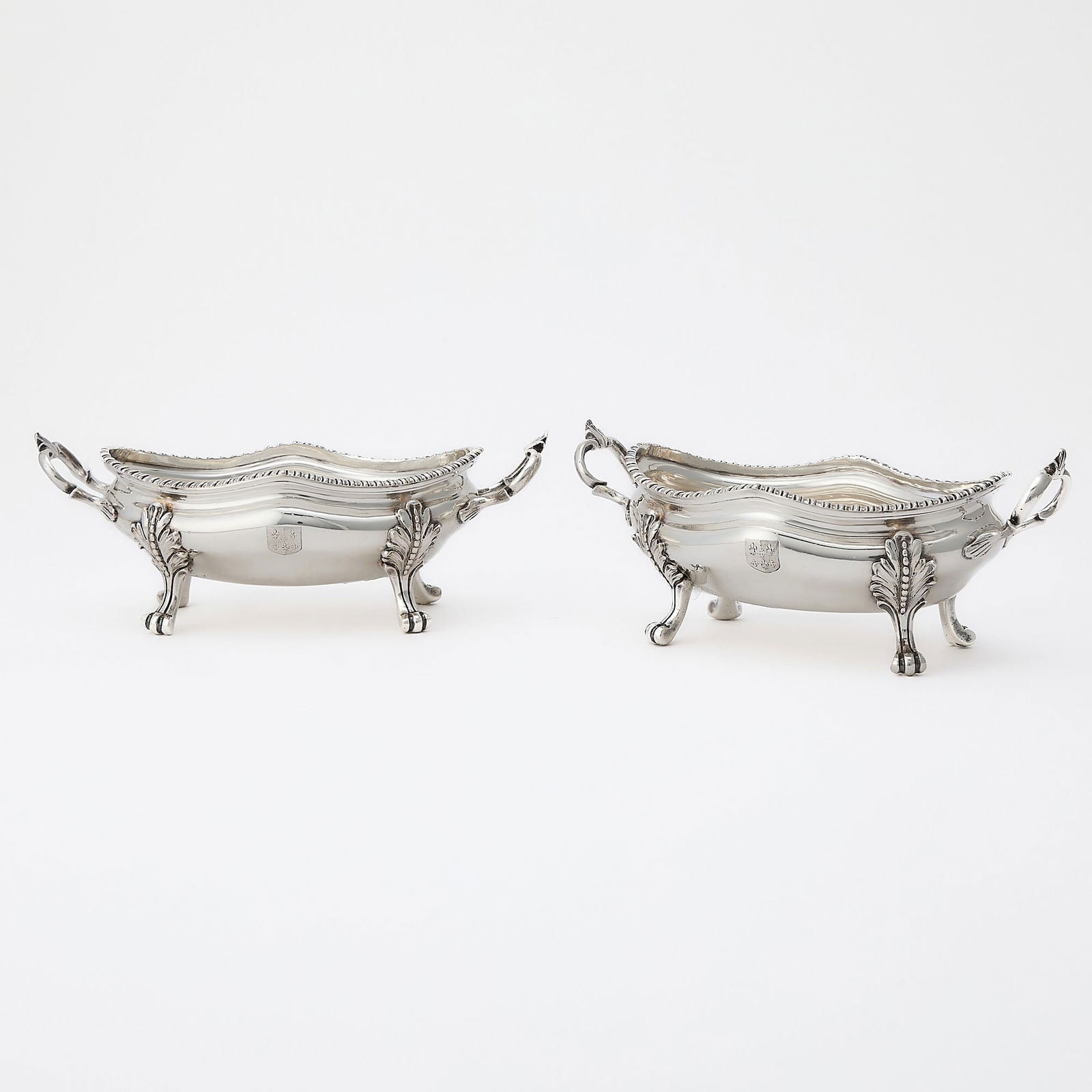 Pair of George III Sterling Silver Sauce Tureens: London, 1765, maker's mark script LH Each oval with gadroon rim, with scrolling loop handles, the feet with foliate joins. Length over handles 9 1/2 inches (24 cm), total approximately 34 ounces. Gen