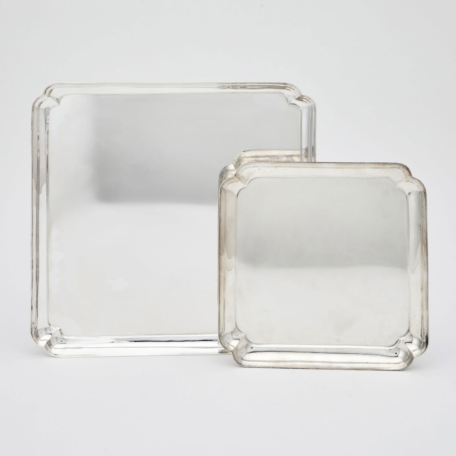 Graduated Pair of Elizabeth II Sterling Silver Salvers: James Robinson, London, 1971 and 1984 Each square with shaped corners, raised on bracket feet. Larger 14 inches (35.5 cm), square, smaller 10 inches (25.5 cm), square, total approximately 89 ounces.