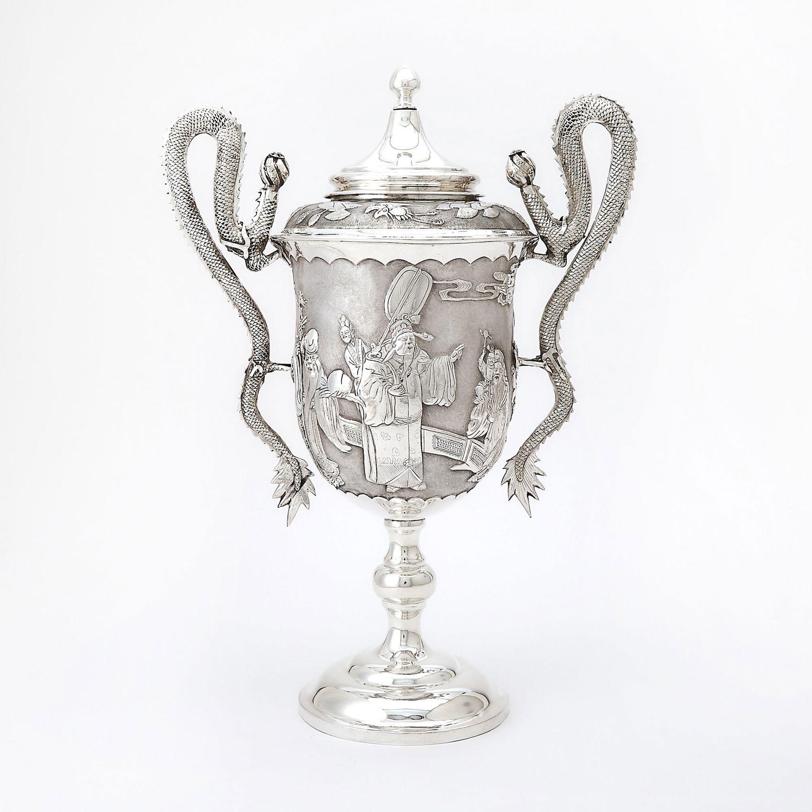 Japanese Export Silver Covered Two-Handled Cup: Late 19th/ early 20th century Goblet-form, the body chased with a figural scene on a knopped stem, with dragon-form handles. Height 16 1/2 inches (42 cm), approximately 44 ounces. With blank shield t