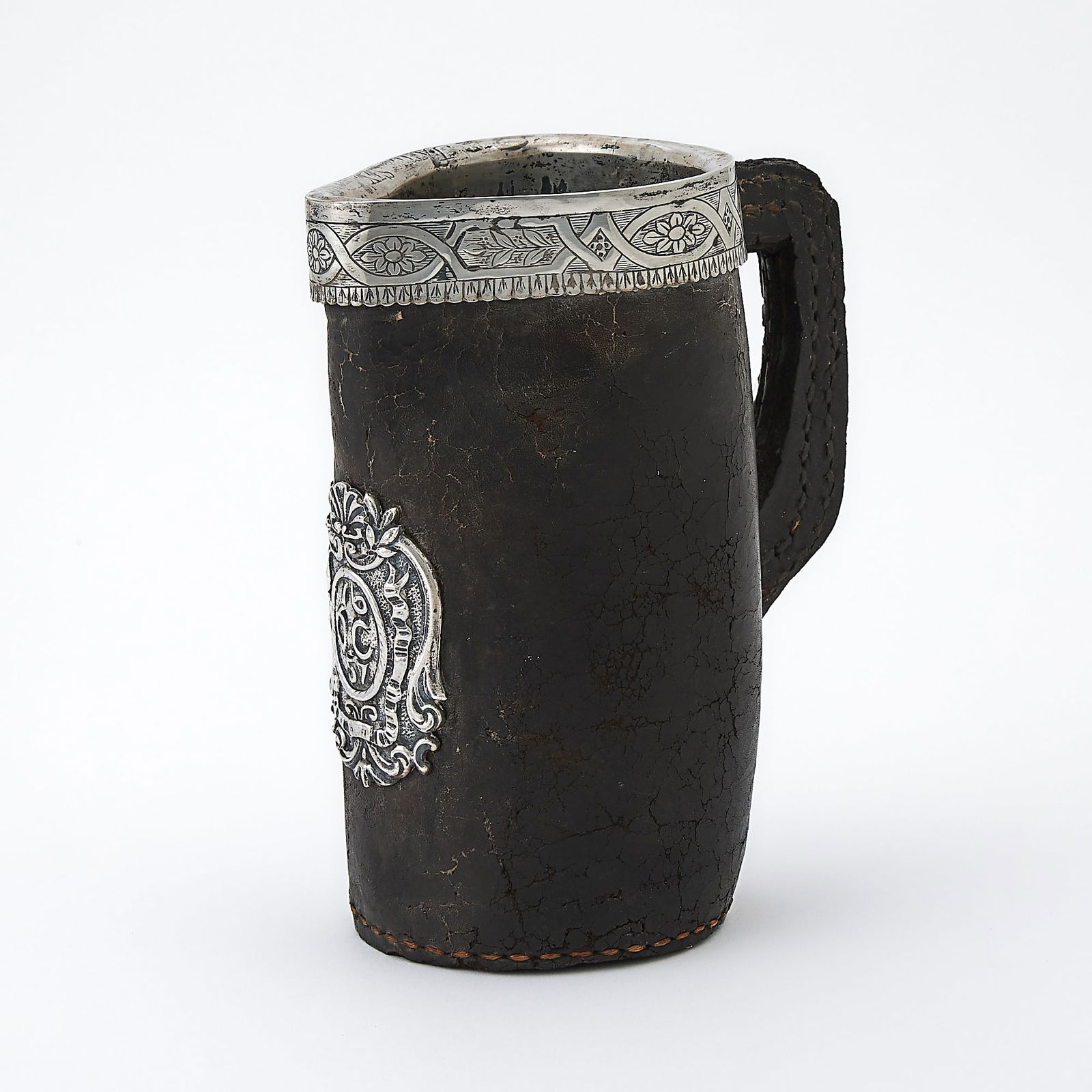 Continental Silvered Metal Mounted Leather Black-Jack Pitcher: Probably 18th century The body applied with a cartouch inscribed "OC 1657". Height 7 1/2 inches (19 cm). Apparently unmarked; the leather dry and cracking; losses to edge of handle; applied cartouch