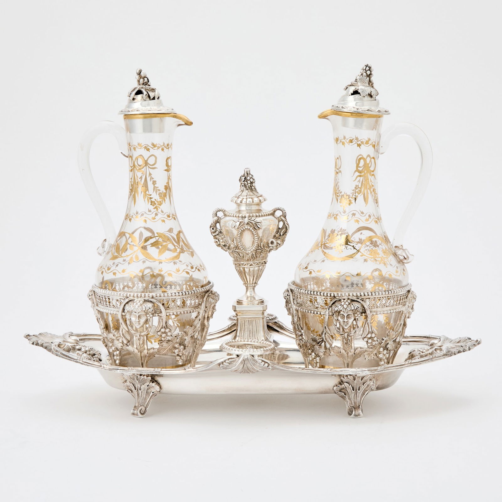 French Silver and Gilt Decorated Glass Cruet Set: Late 19th/early 20th century In the Louis XVI style, the shaped oval body with tied reeded border and shell-form ends, fitted with two rings with bacchaic masks and swags of grape leaves and clusters