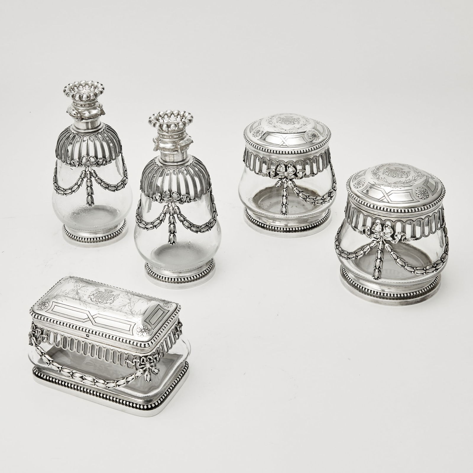 French Silver and Glass Part Dresser Set: Aucoc, Paris, early 20th century The mounts with husk swags, comprising a pair of bottles, height 6 7/8 inches (17 cm), pair of circular boxes, diameter 4 inches (10 cm), and a rectangular box, lengt