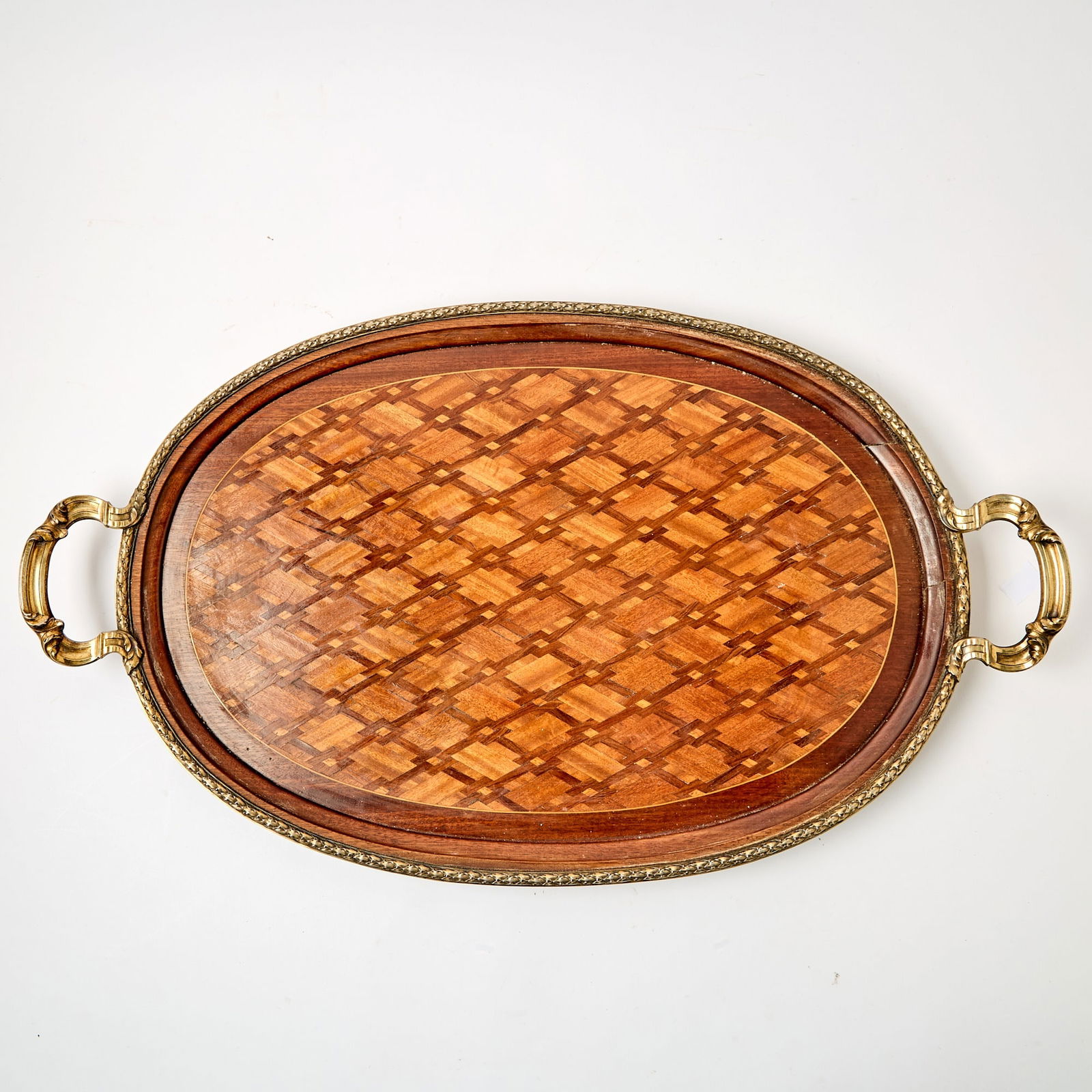 French Silver Mounted Parquetry Two Handled Tray: First half 20th Century Oval with parquetry inlay forming a repeating diamond pattern in various contrasting woods, borderd by a molded wood edge, enclosed within a silver gallery rim applied with
