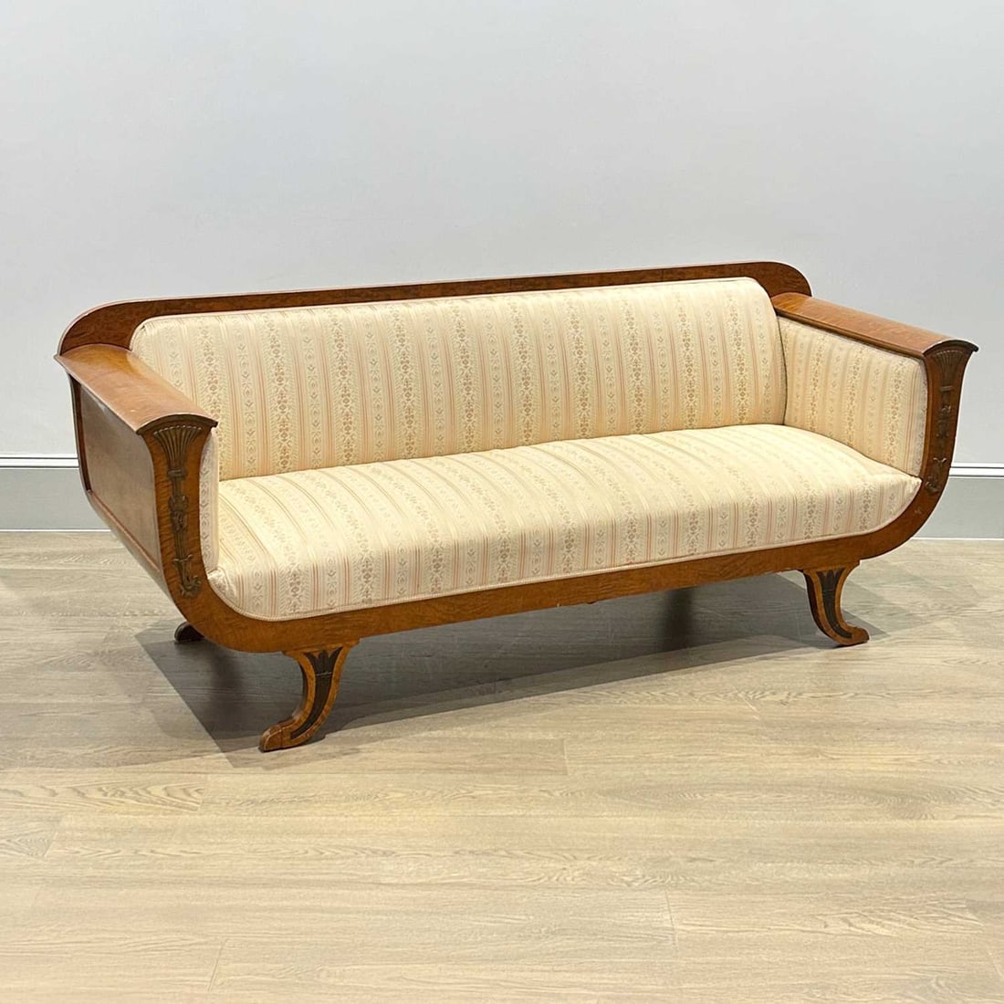 Biedermeier Maple Upholstered Sofa: 19th centuryThe slightly arched crest above similarly shaped arms with flat fronts and applied floral devices, raised on flaring feet.Length 7 feet 1 inch, depth 28 inches.