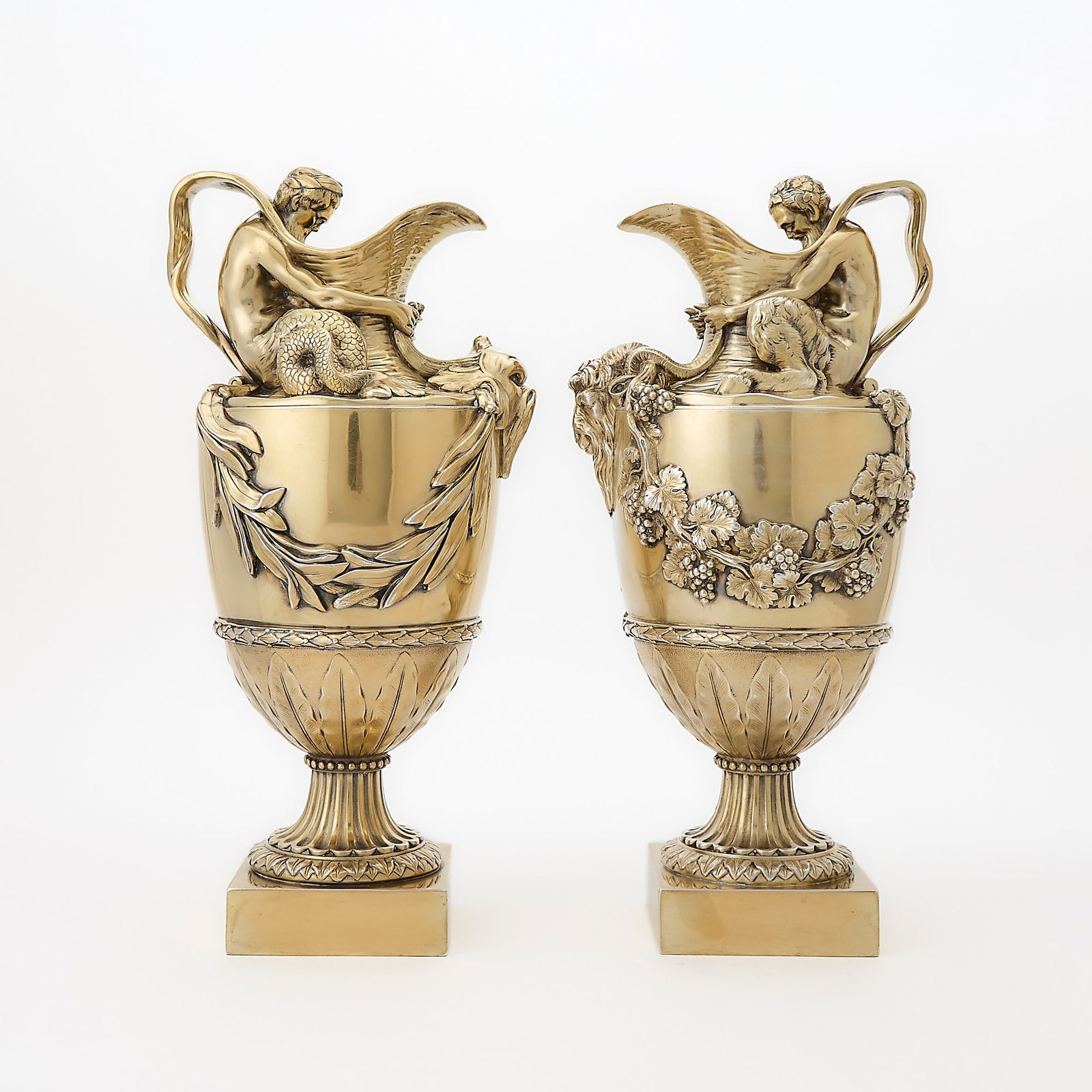 Pair George V Sterling Silver-Gilt Wine and Water Ewers: Sydney Bellamy Harman, London, 1910 The water ewer depicting a triton wrapping arms around the spout and holding a dolphin's fins, the wine ewer depicting a satyr, wrapping arms around the spout and p