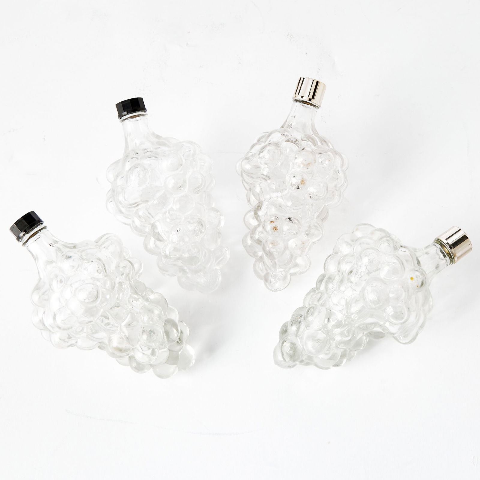 Group of Twenty-Four French Molded Glass Grape-Form Bottles: Mid 20th CenturyEach formed as a bunch of grapes, in colorless glass, molded BOTTLE MADE IN FRANCE. Length 6 1/2 inches.(24)