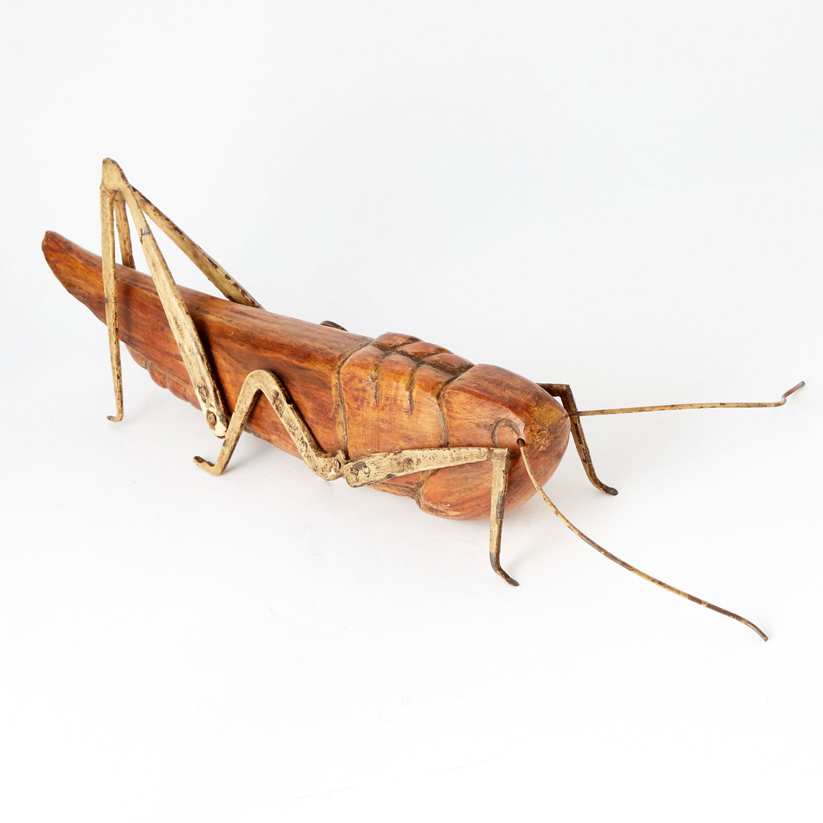 Spanish Carved Wood Figure of a Grasshopper: With painted metal legs and antenna, labeled Made in Spain.Height 8 inches, length overall 29 1/2 inches.