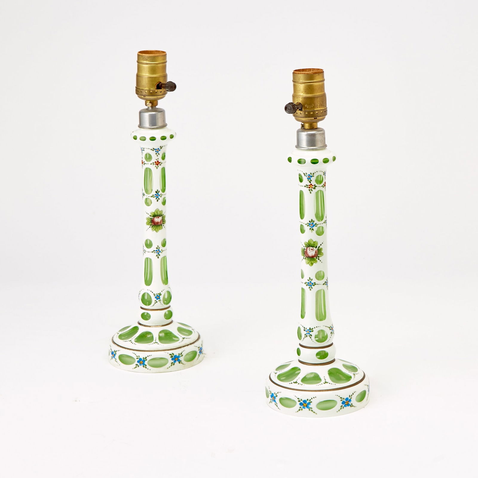 Pair of Bohemian Style Overlay Glass Candlestick Lamps: 20th Century Each of circular columnar form, in transparent green colored glass cased in opaque white, painted with red rose blossoms, blue blossoms, and green leaves. Height of body 11 inches.