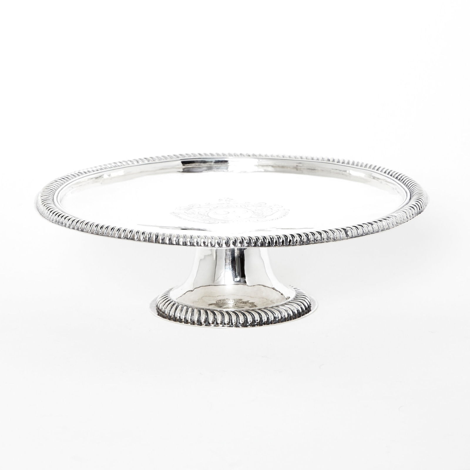Queen Anne Sterling Silver Tazza: London, 1704 Circular with gadrooned border, the center engraved with heraldic arms, raised on a trumpet-form foot. Height 3 inches, diameter 9 3/4 inches, approximately 15 ounces. Provenance: I. Fran