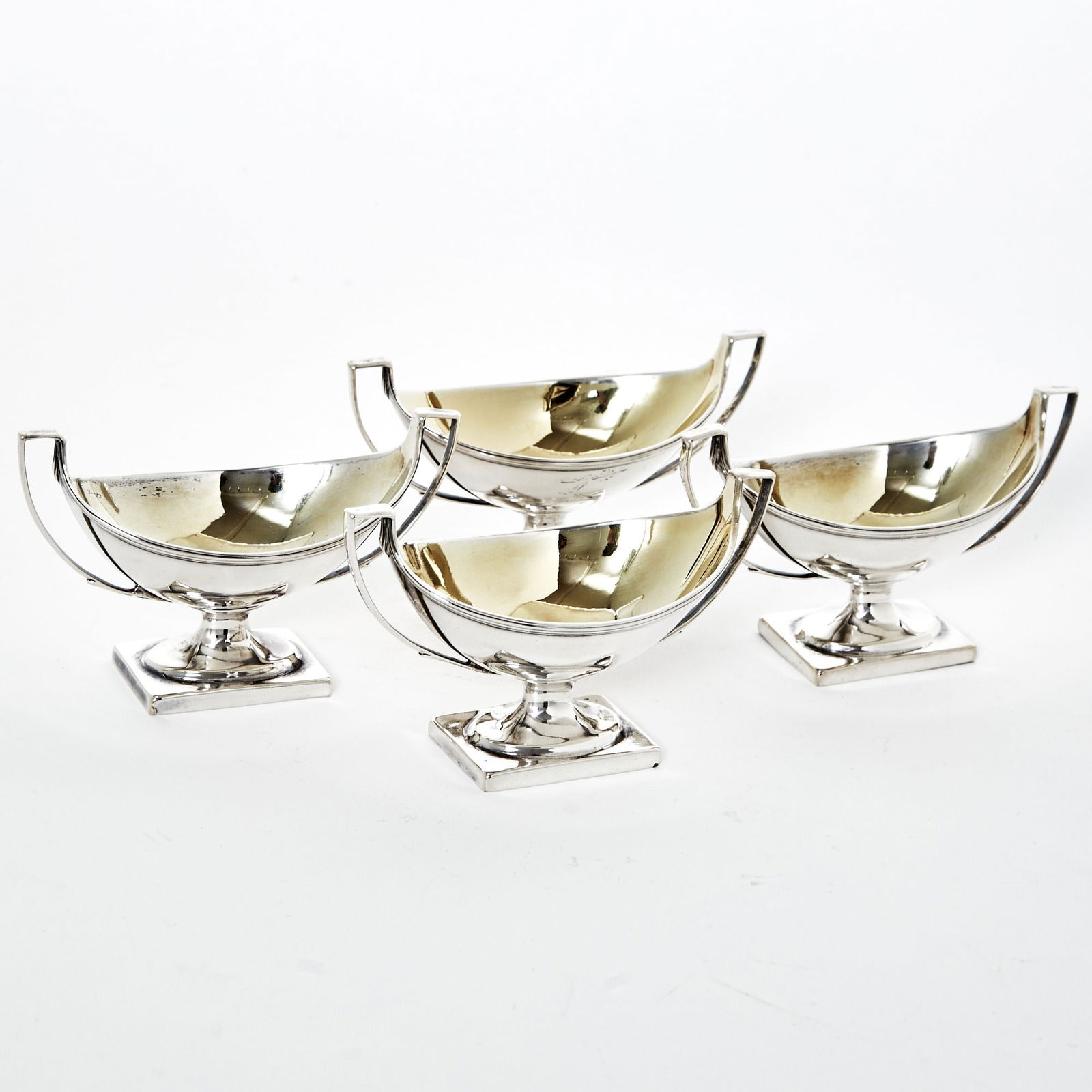 Set of Four George III Sterling Silver Open Salt Cellars: Peter Podio, London, 1791 Each oval with reeded border and angular loop handles, on a rectangular base. Length over handles 5 inches, total approximately 13 ounces. Provenance: William Walter, London,