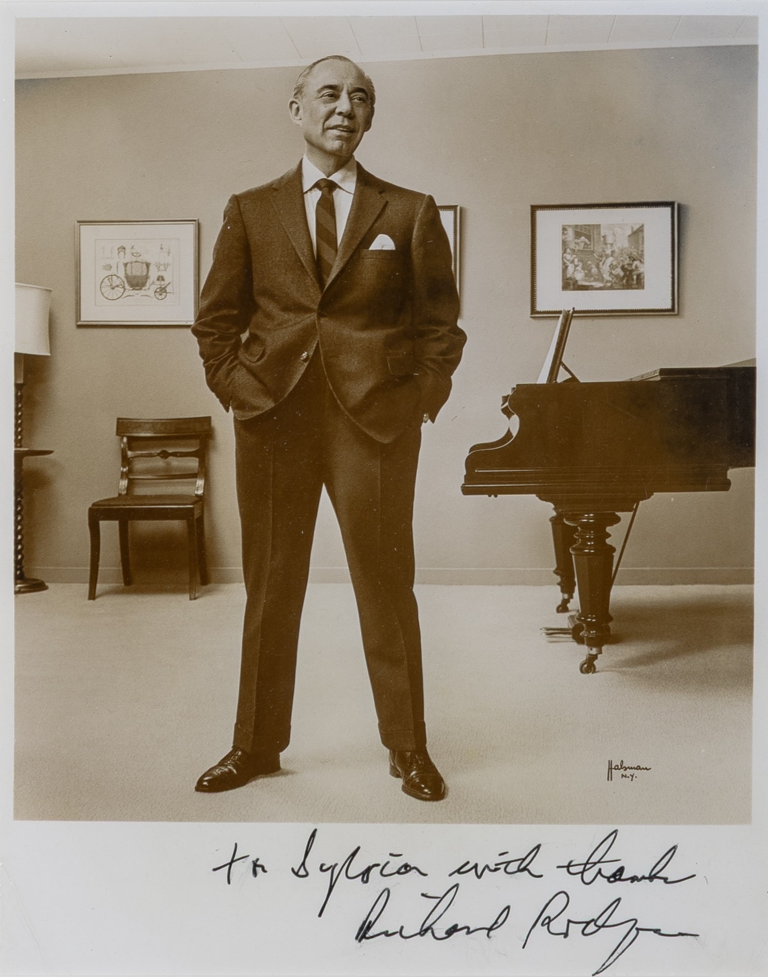 A fine photograph inscribed by Richard Rodgers: RICHARD RODGERSInscribed photograph. A sepia toned print depicting Richard Rodgers in full length before a piano, inscribed below the image "To Sylvia with thanks/ Richard Rodgers." The photograph by