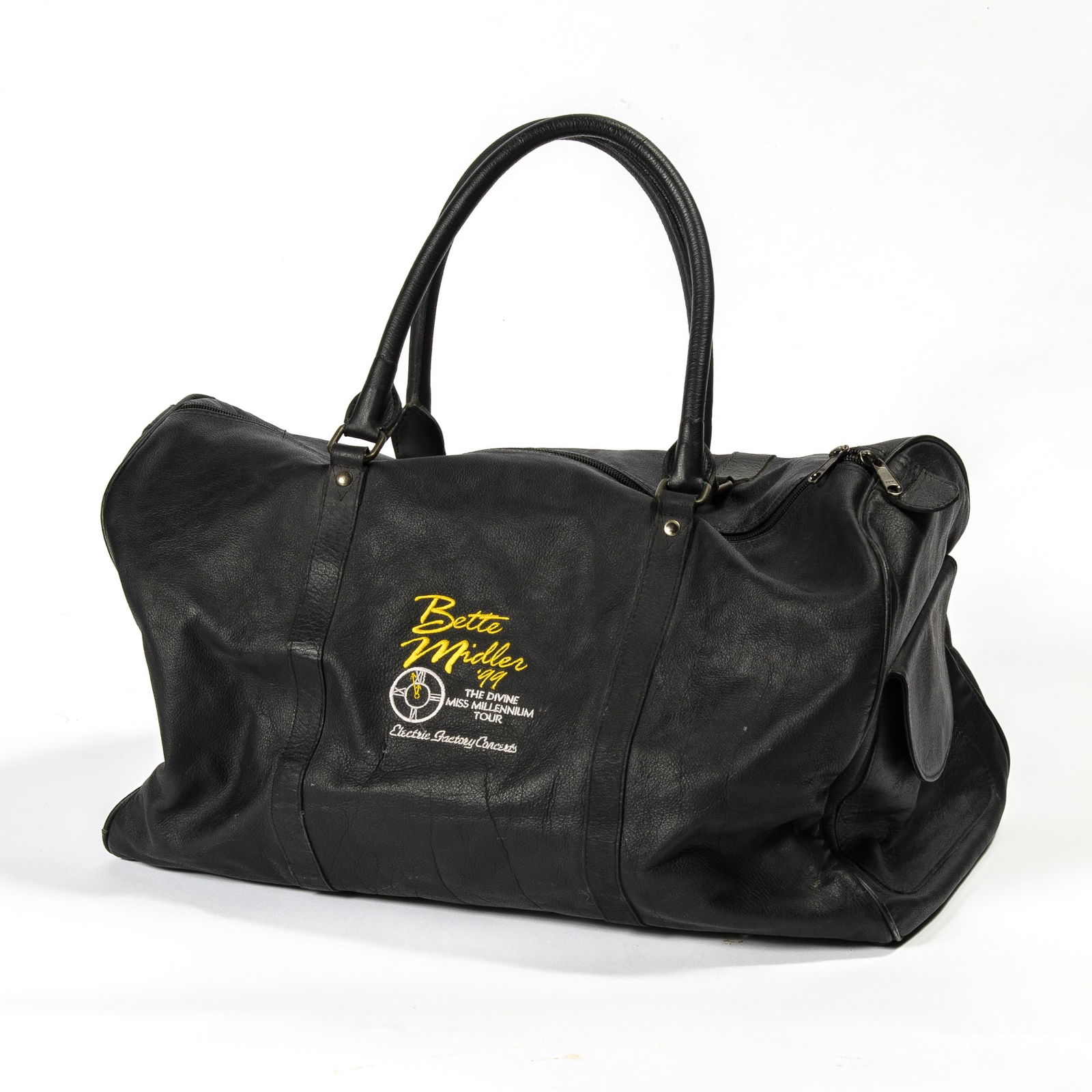 A collection of memorabilia from Bette Midler's The Divine Miss Millennium Tour: BETTE MIDLER A collection of memorabilia from Bette Midler's The Divine Miss Millennium Tour. Circa 1999. Comprising a branded black leather weekender bag, an engraved Tiffany bracelet, and a "I flas