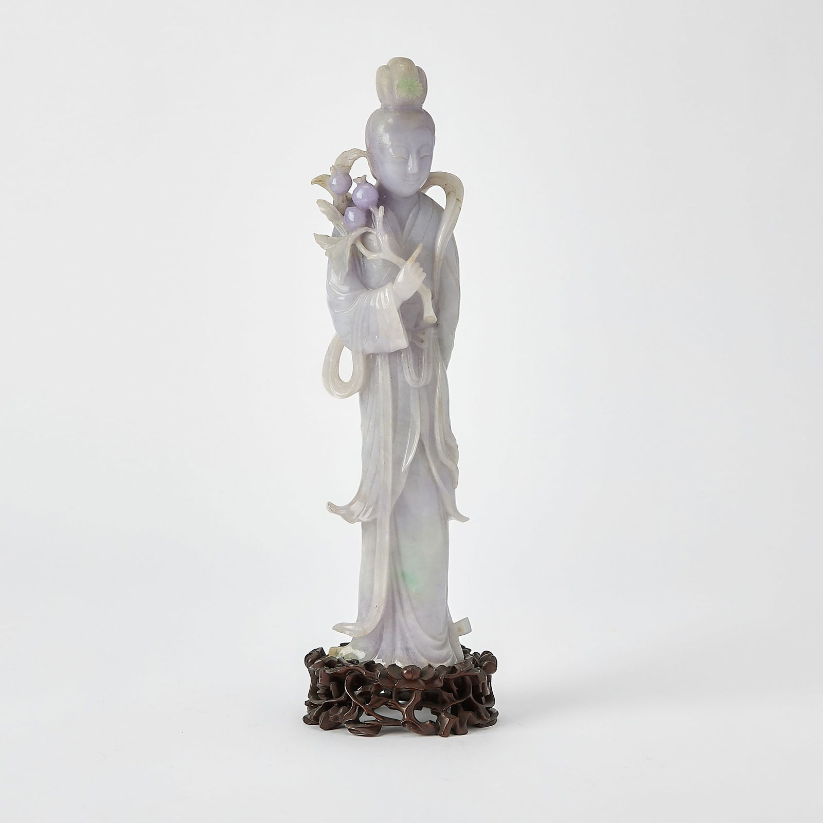 A Chinese Lavender Jadeite Figure of a Meiren Late Qing Dynasty: Carved as a slender meiren dressed in long, flowing robes, holding a pomegranate stem and a scythe behind her back, the face with a pleasant expression beneath a high chignon. (Height 12 1/4 inches)