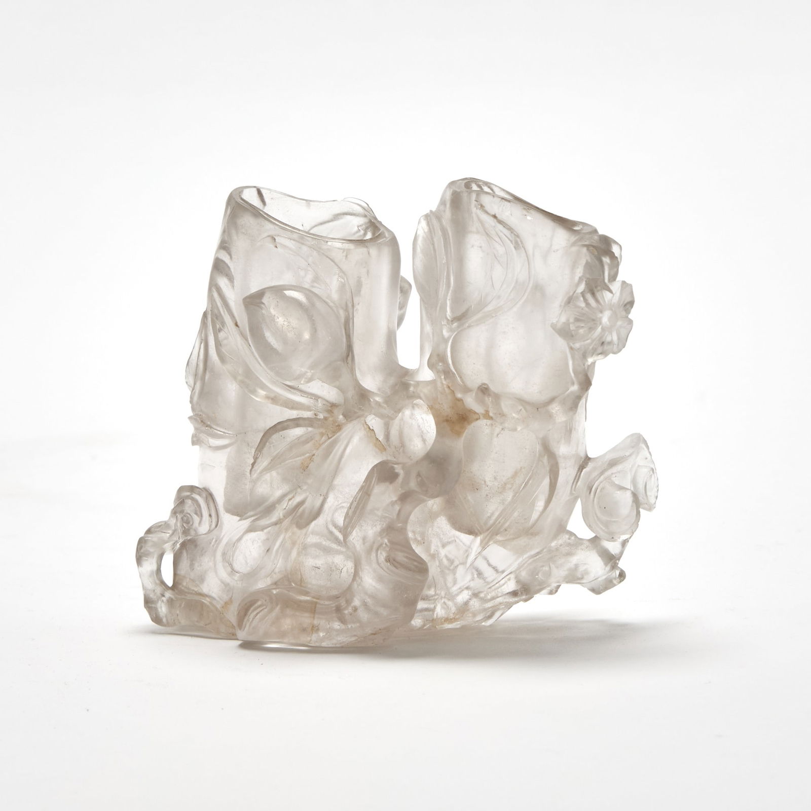 A Chinese Rock Crystal Brush Pot Qing Dynasty: Modeled as a splitting, gnarled trunk surrounded by peaches, lingzhi, and blossoms on leafy branches. (Height 4 inches) A few chips and nicks at rims (see photos).