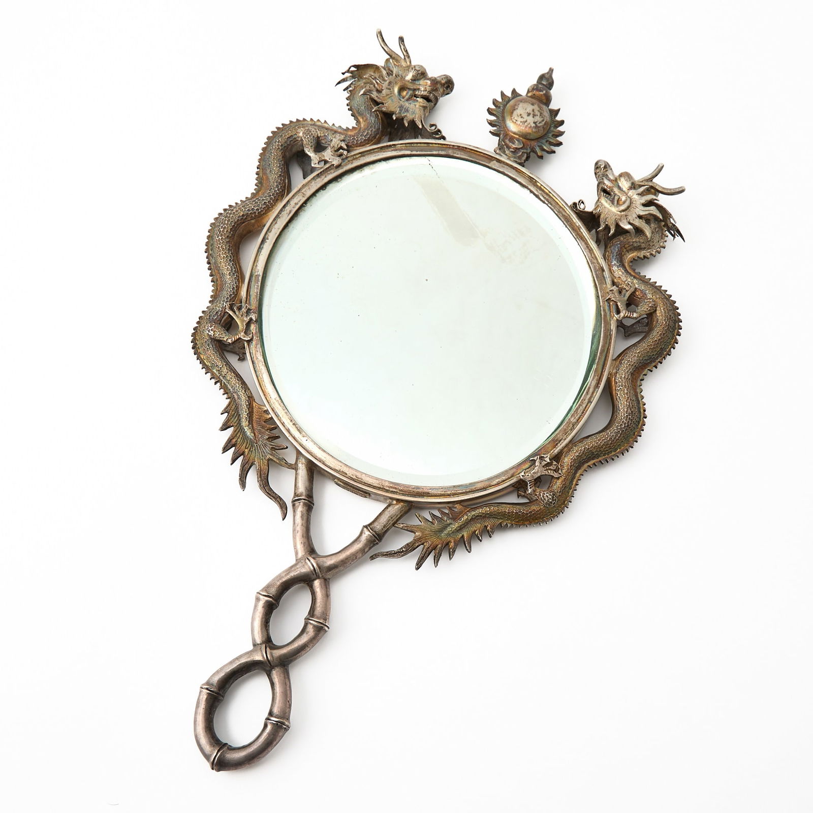 A Chinese Silver Hand Mirror 19th century: The circular mirror framed with a pair of confronting dragons chasing a pearl, the handle decorated as twisted bamboo. (Length 12 1/2 inches)
