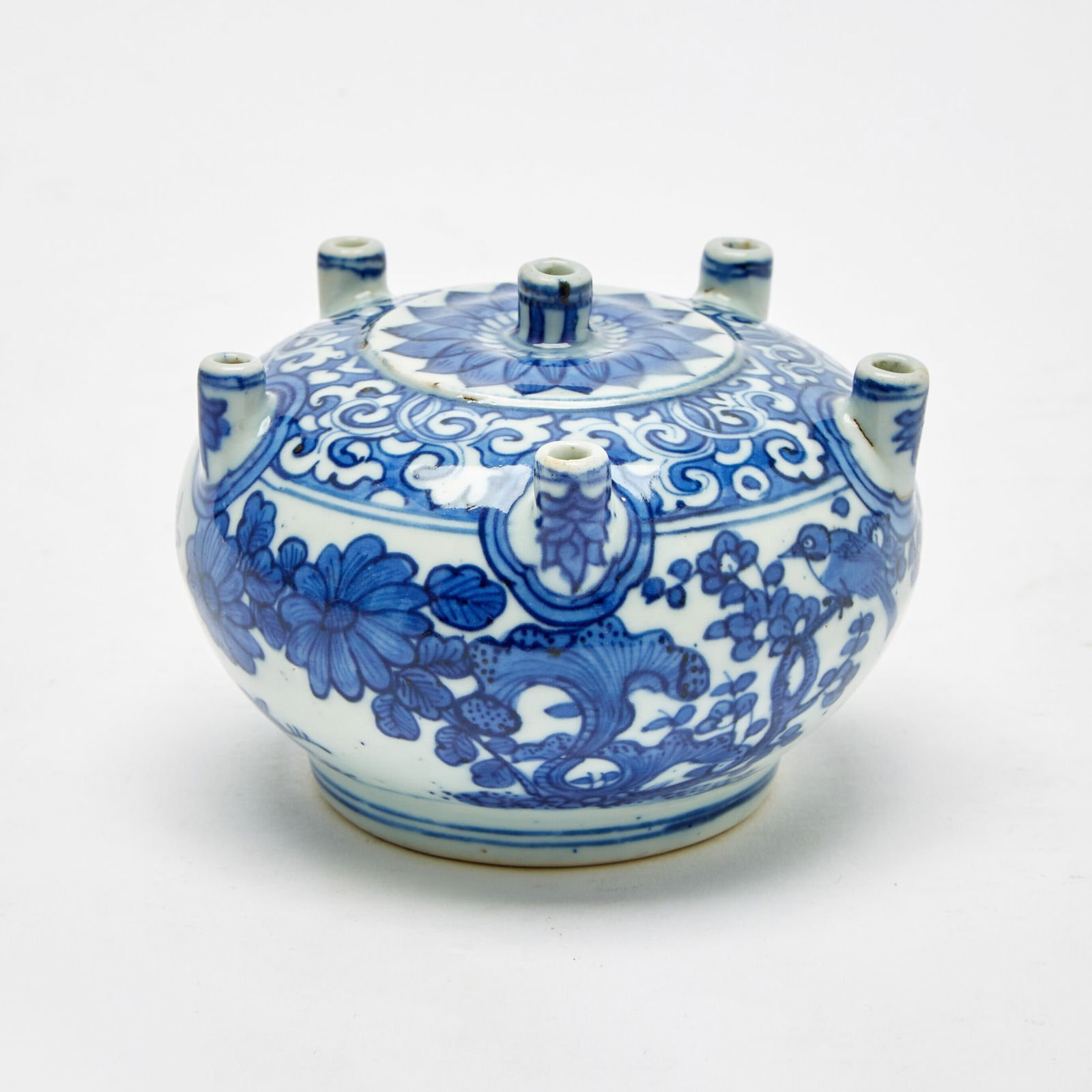 An Unusual Chinese Blue and White Porcelain Multi-Spouted Vase Wanfu Youtong Mark, Wanli Period: Of compressed globular form, the body raised on a straight foot and surmounted by six short cylindrical spouts; decorated with blossoms borne on leafy branches, along with a bird, insects and foliage;
