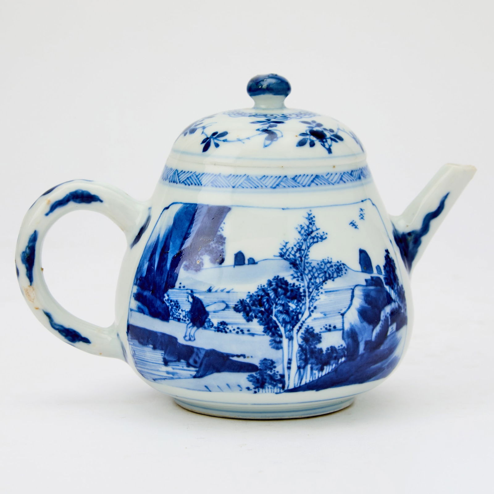 A Chinese Blue and White Porcelain Teapot Kangxi Period: Of tapering form with a domed top, straight spout, and a curved handle; decorated with shaped panels depicting figures within landscapes. (Height 5 1/2 inches) Chait Galleries, New York; with label.