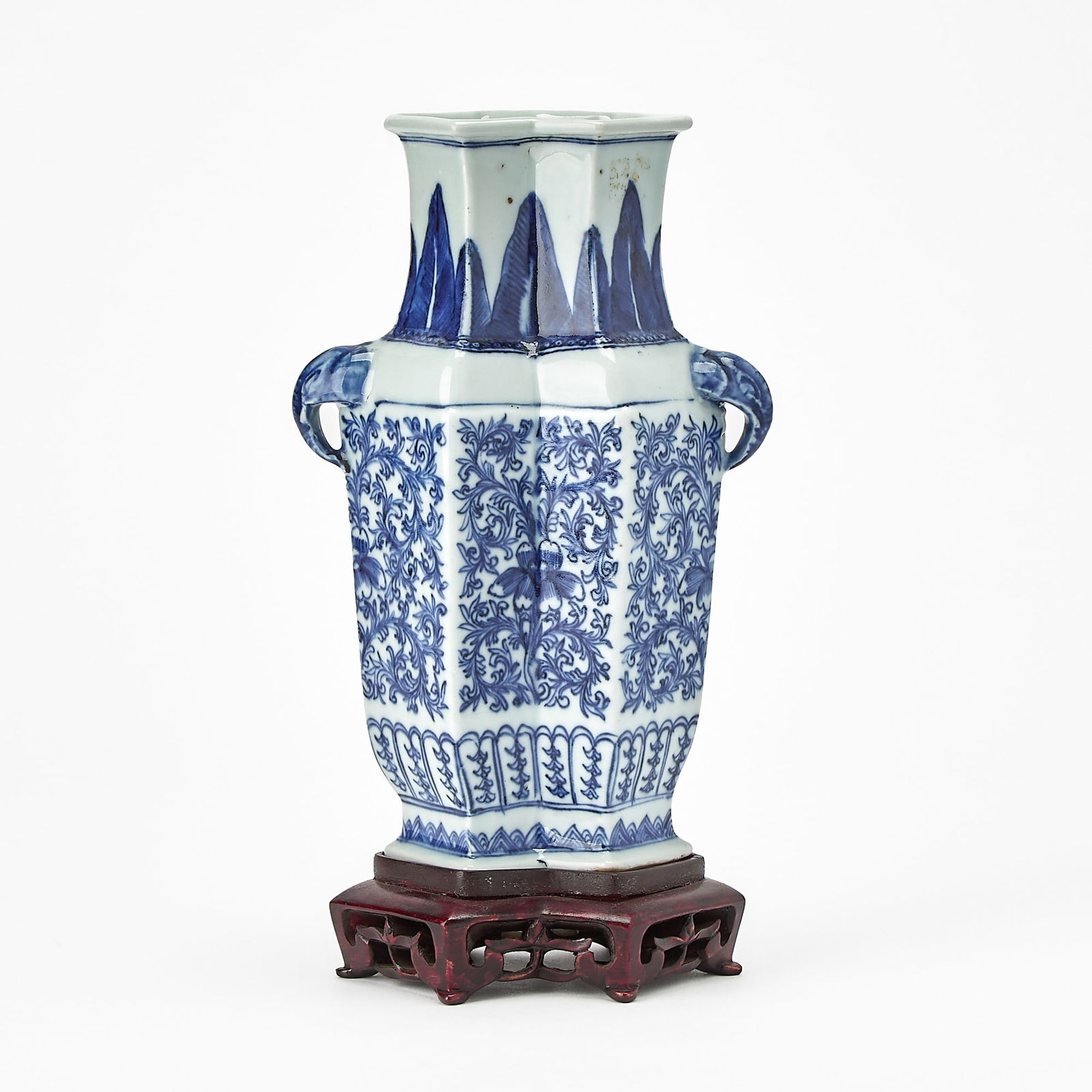 A Chinese Blue and White Porcelain Lozenge-Shaped Vase 18th century: Modeled with a pair of elephant-head handles; the exterior decorated with scrolling lotus, all between lappet bands at the neck and base; with a later fitted stand. (Height 8 3/4 inches)