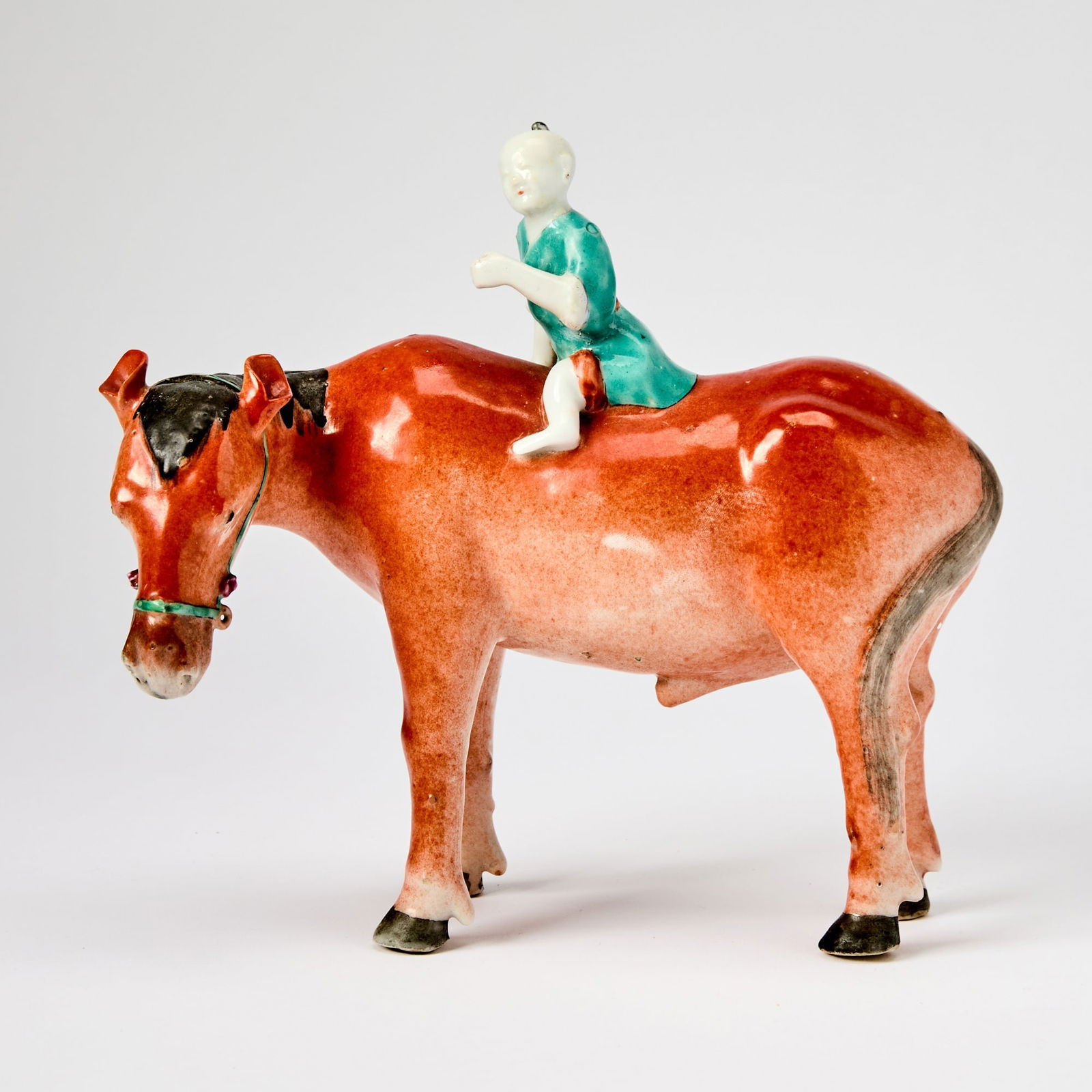 A Chinese Enameled Porcelain 'Boy on Horse' Figural Grouping 19th Century: Modeled as a boy astriding a four-square horse with its head turned to the left. (Length 7 1/4 inches)