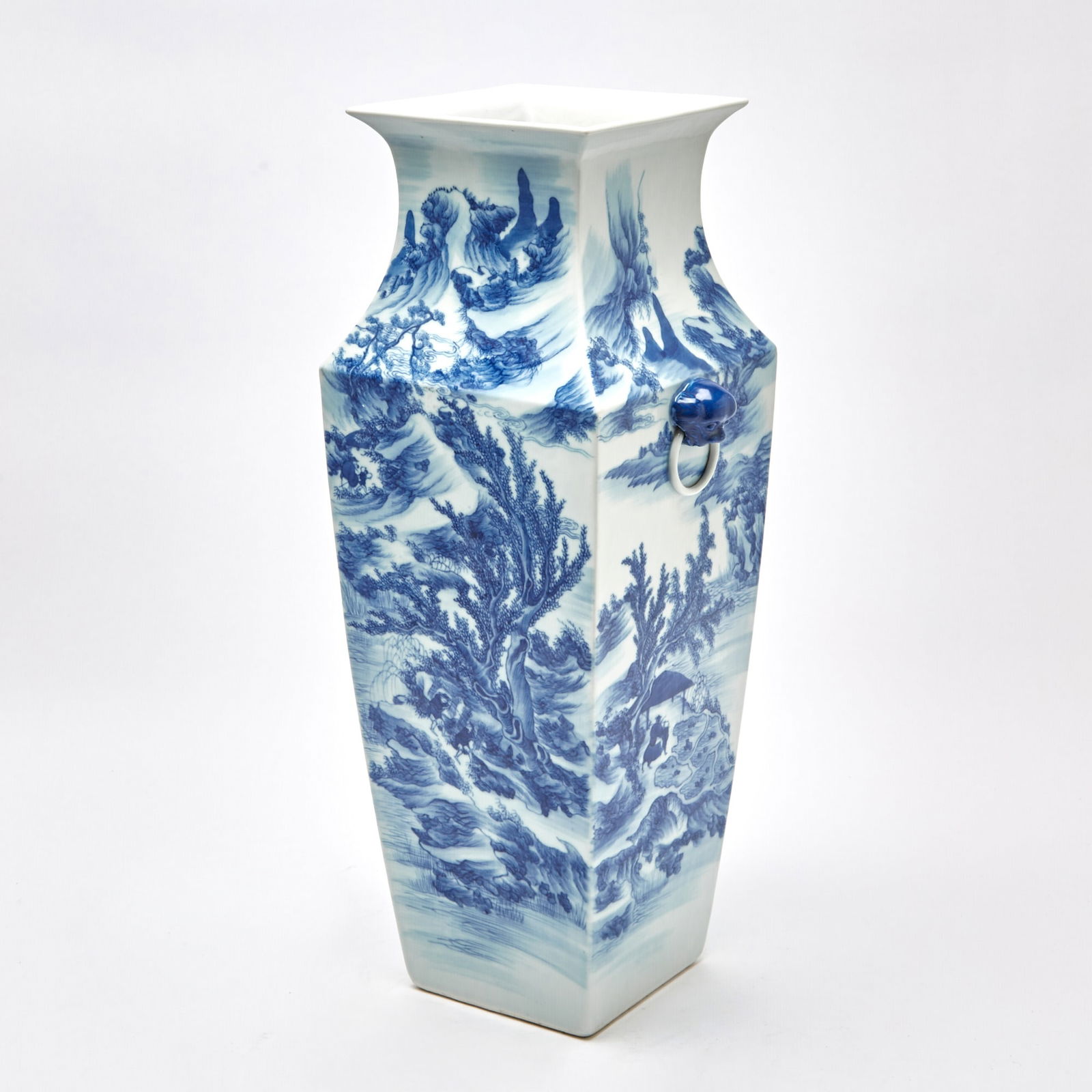 A Large Chinese Blue and White Porcelain Square Vase 19th Century: The tapering rectangular body with a faceted flaring neck, decorated with a pair of handles in the form of heads of fu lions, with rings issuing from their mouths; the exterior adorned with scholars a