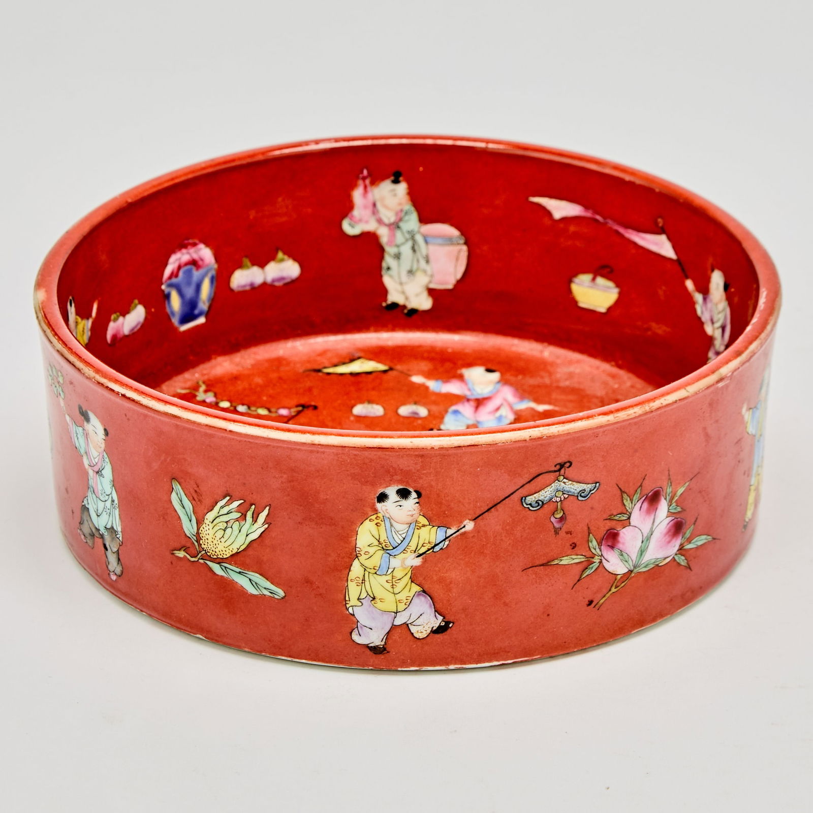A Chinese Enameled Red Ground Porcelain ‘Boys’ Bowl Jiaqing Mark, Qing Dynasty: Of shallow, circular form; decorated with 'boys at play' over a copper red ground. (Diameter 7 inches)