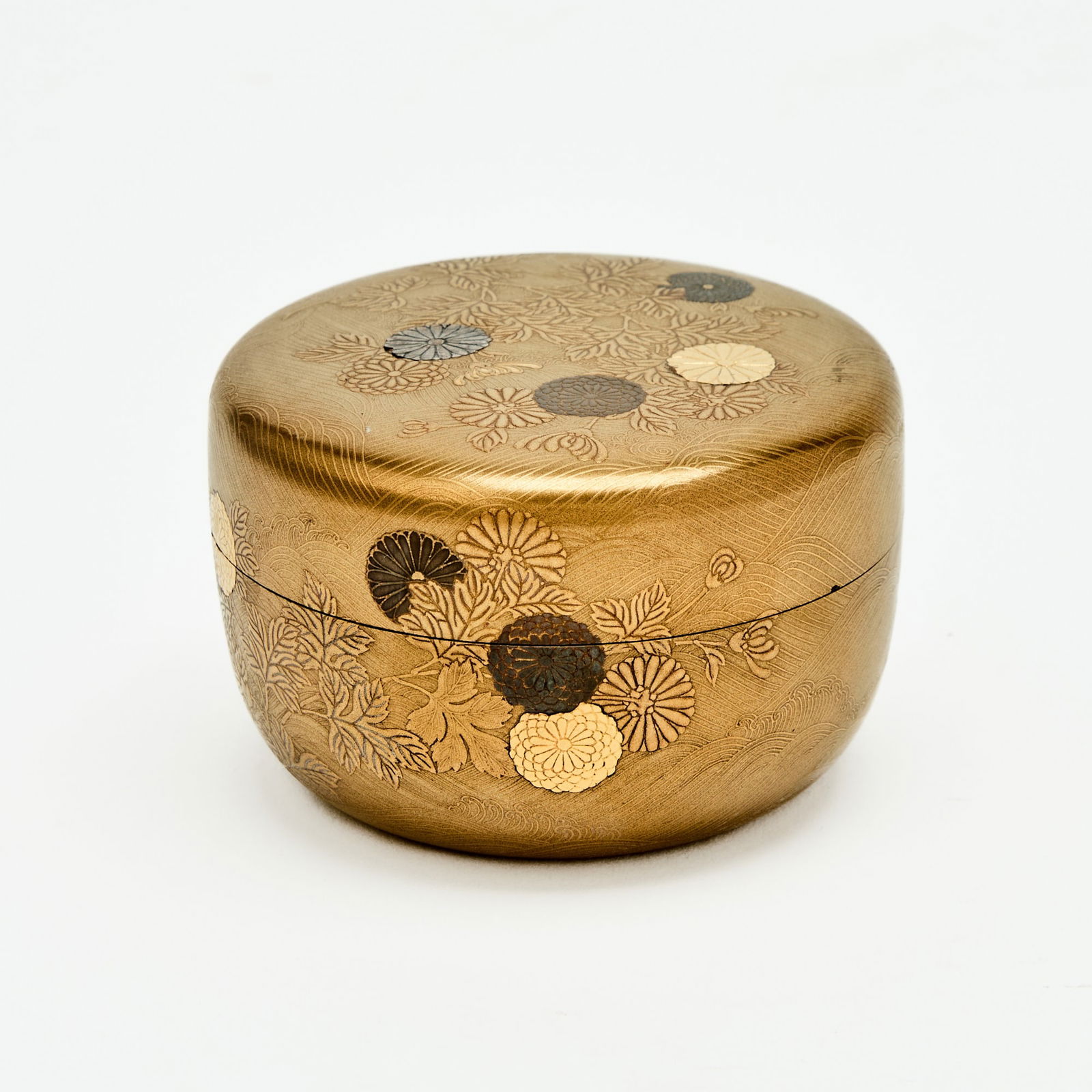 A Japanese Black and Gilt Lacquer Tea Caddy Edo-Meiji Period: Carved and decorated with chrysanthemum blossoms borne on leafy branches against a ground of crashing waves. (Diameter 3 1/4 inches)