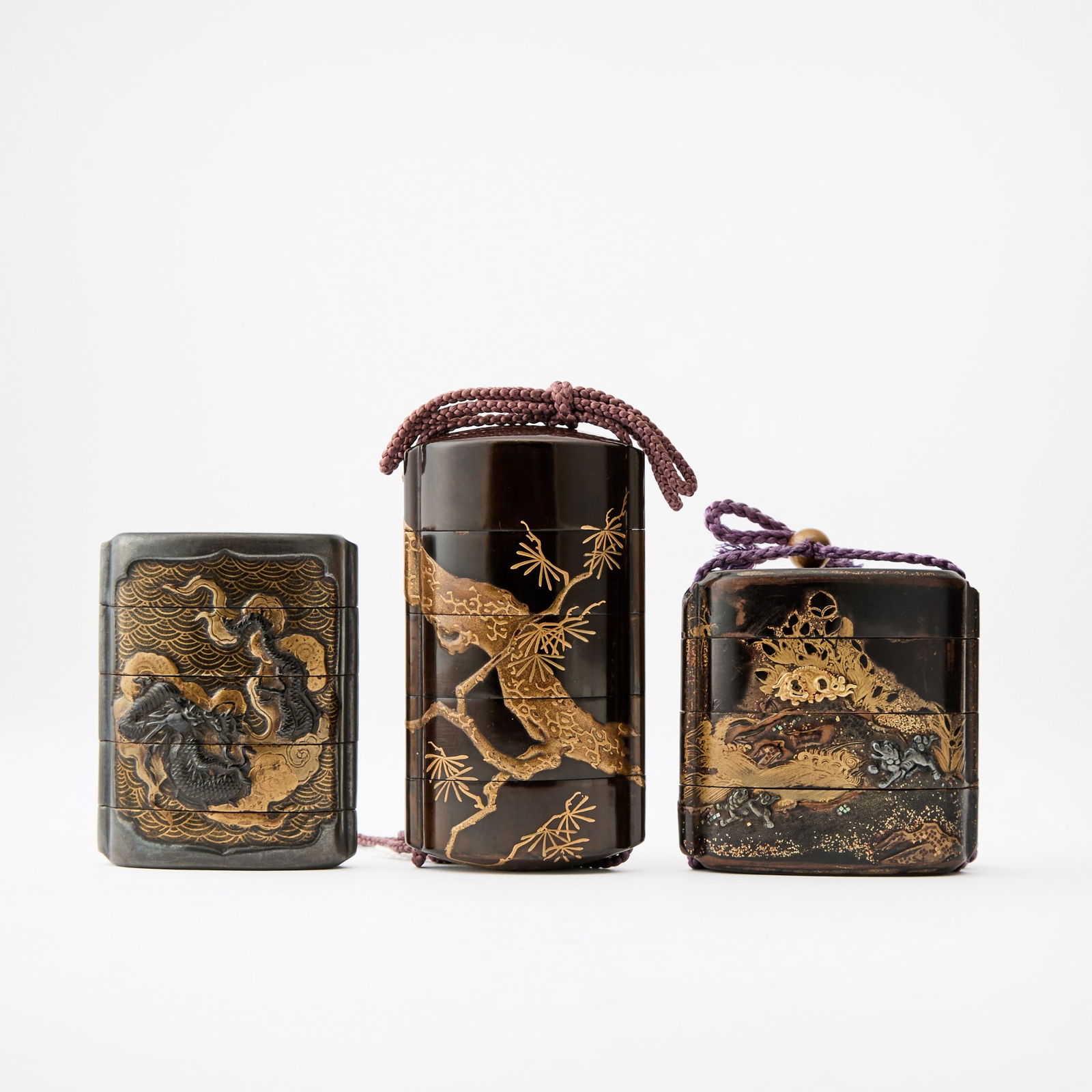 Three Japanese Black and Gilt Lacquered Inro 19th Century: One decorated with a dragon amid stylized waves, one with a pine branch, and one depicting mythical beasts in a mountainous landscape. (Height of largest 3 1/2 inches)