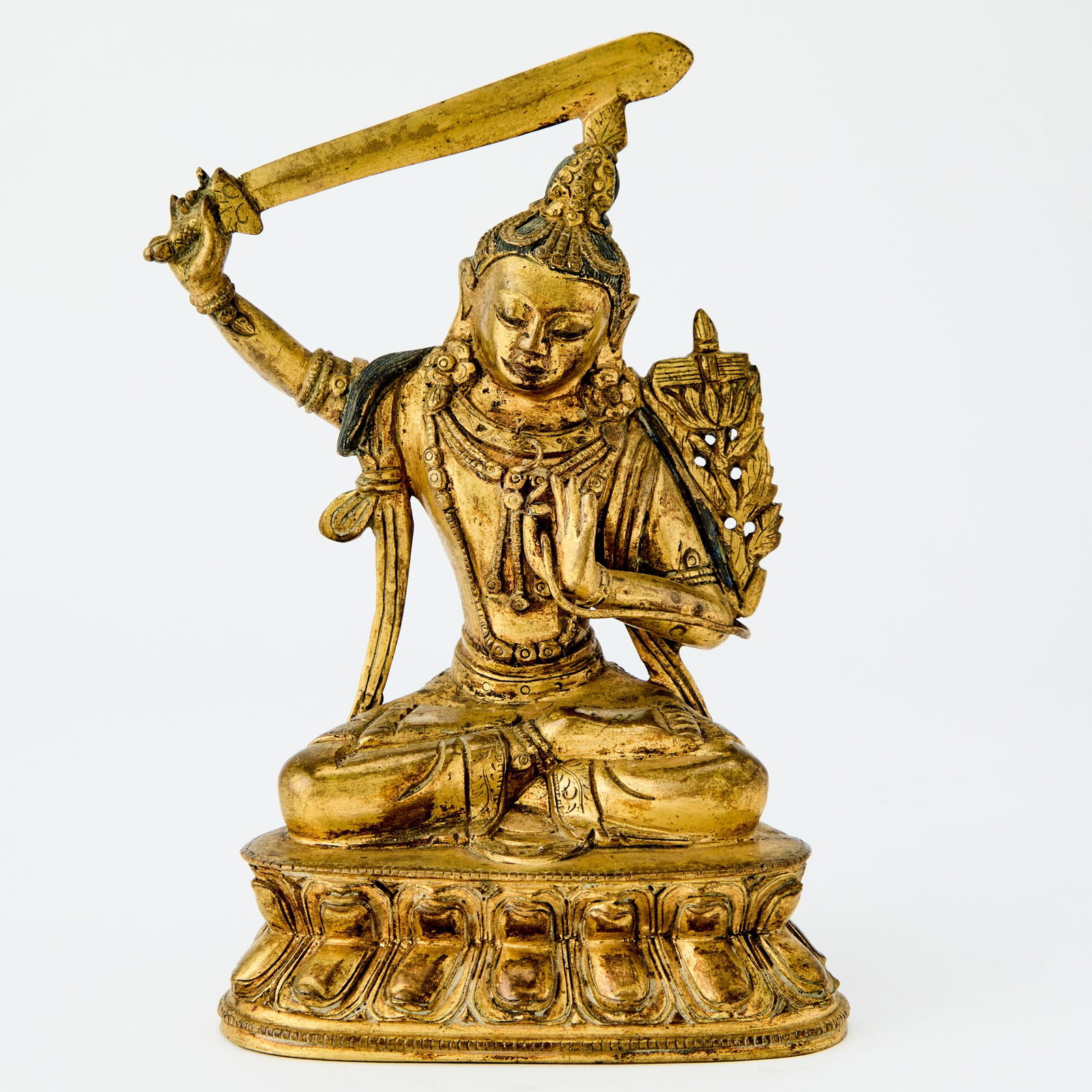 A Sino-Tibetan Gilt Bronze Figure of Manjushri 18th Century or Later: Cast as a seated figure with legs crossed in dhyanasana on a double-lotus base, the right hand holding a sword raised above the head and the left hand in the gesture of varada mudra. (Height 6 3/4 inc