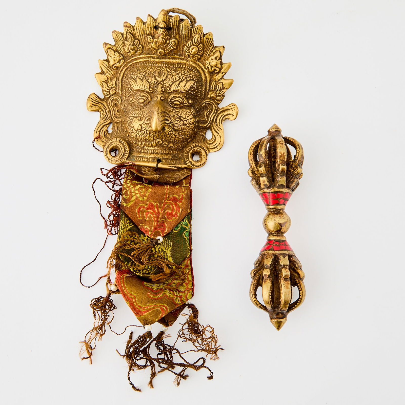Two Tibetan Gilt Bronze Articles 18th-19th century: Comprising a flanged vajra inset with red stones and a bronze mask of Garuda with brocade silk ribbon. (Length 5 inches)