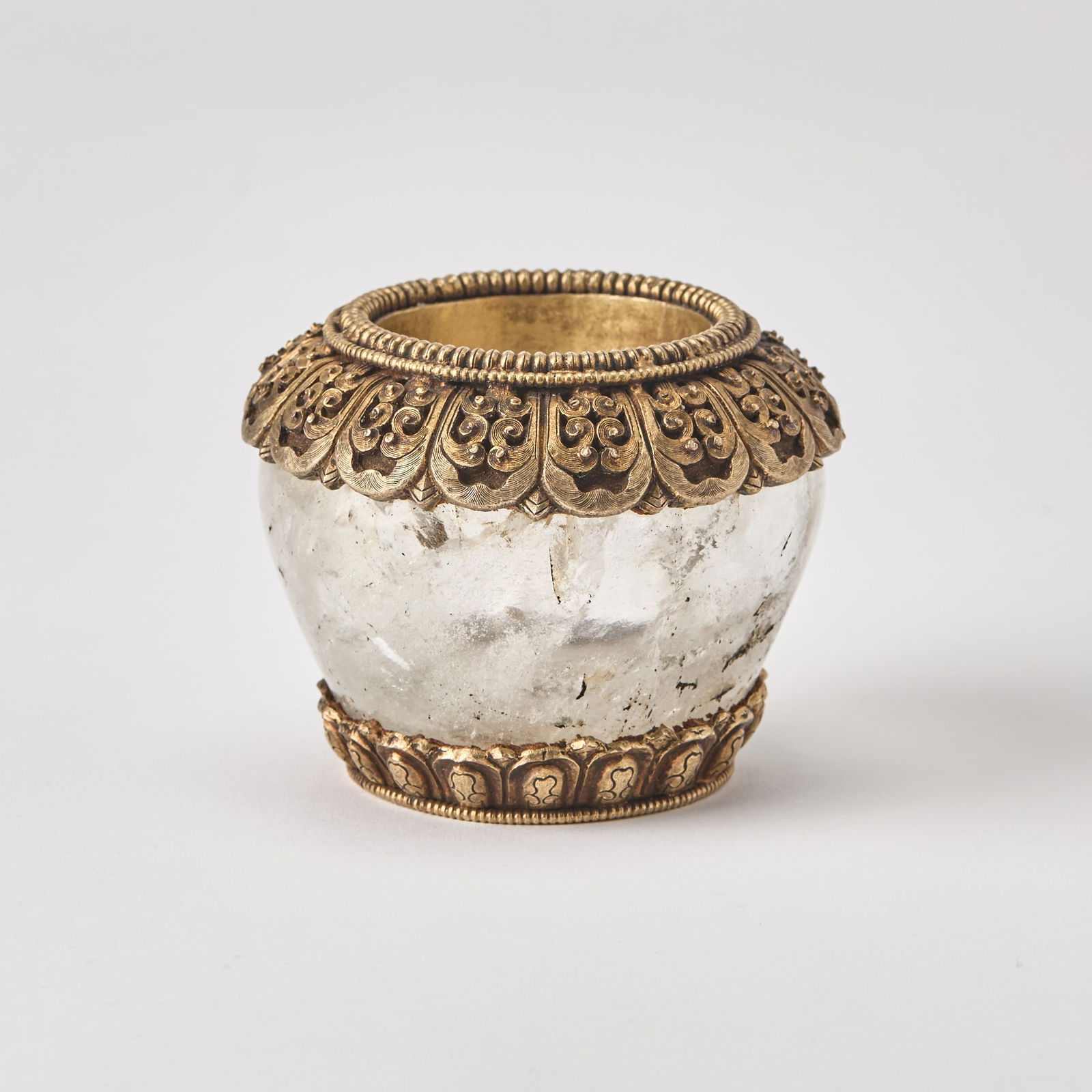A Tibetan Gilt-Bronze-Mounted Rock Crystal Bowl 19th century: The ovoid bowl tapering to narrow foot partially clad in Chinese-style gilt copper alloy bands. (Height 2 3/4 inches)