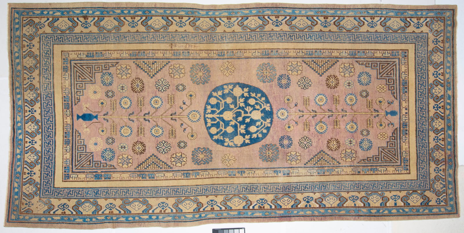 Khotan Carpet 19th Century: East Turkestan, Circa 1900 The central circular medallion flanked by pomegranates on the pale plum field is within a saffron cloud and wave border. (13' 0" x 6' 5") Areas of wear, re-wrapped selvedges