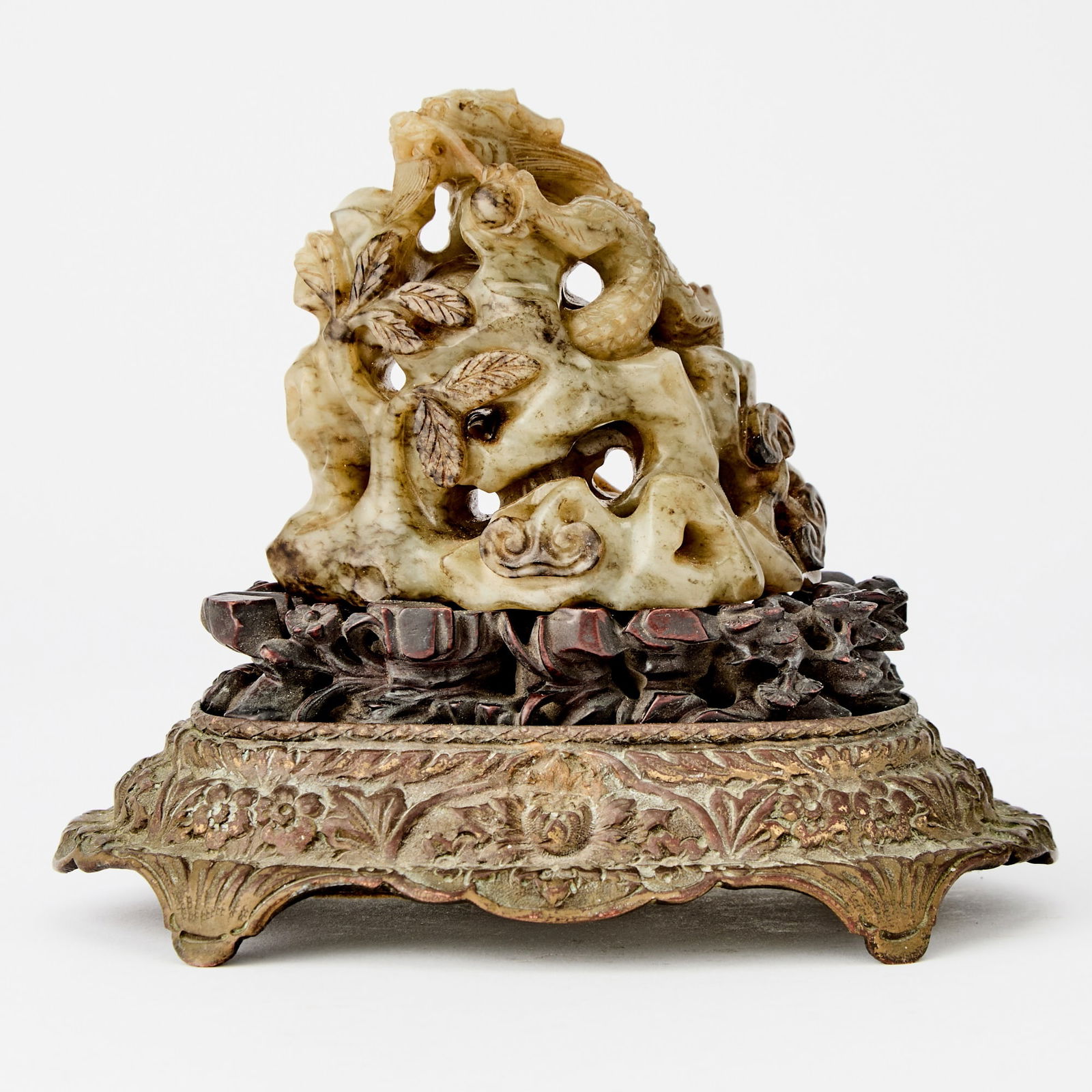 A Chinese Carved Openwork Jade Finial Qing Dynasty: Carved in openwork to depict a chilong clambering amidst pierced rockwork issuing branches and lingzhi fungus; mounted on a carved wood stand above a gilt-metal base. (Length 3 1/4 inches)
