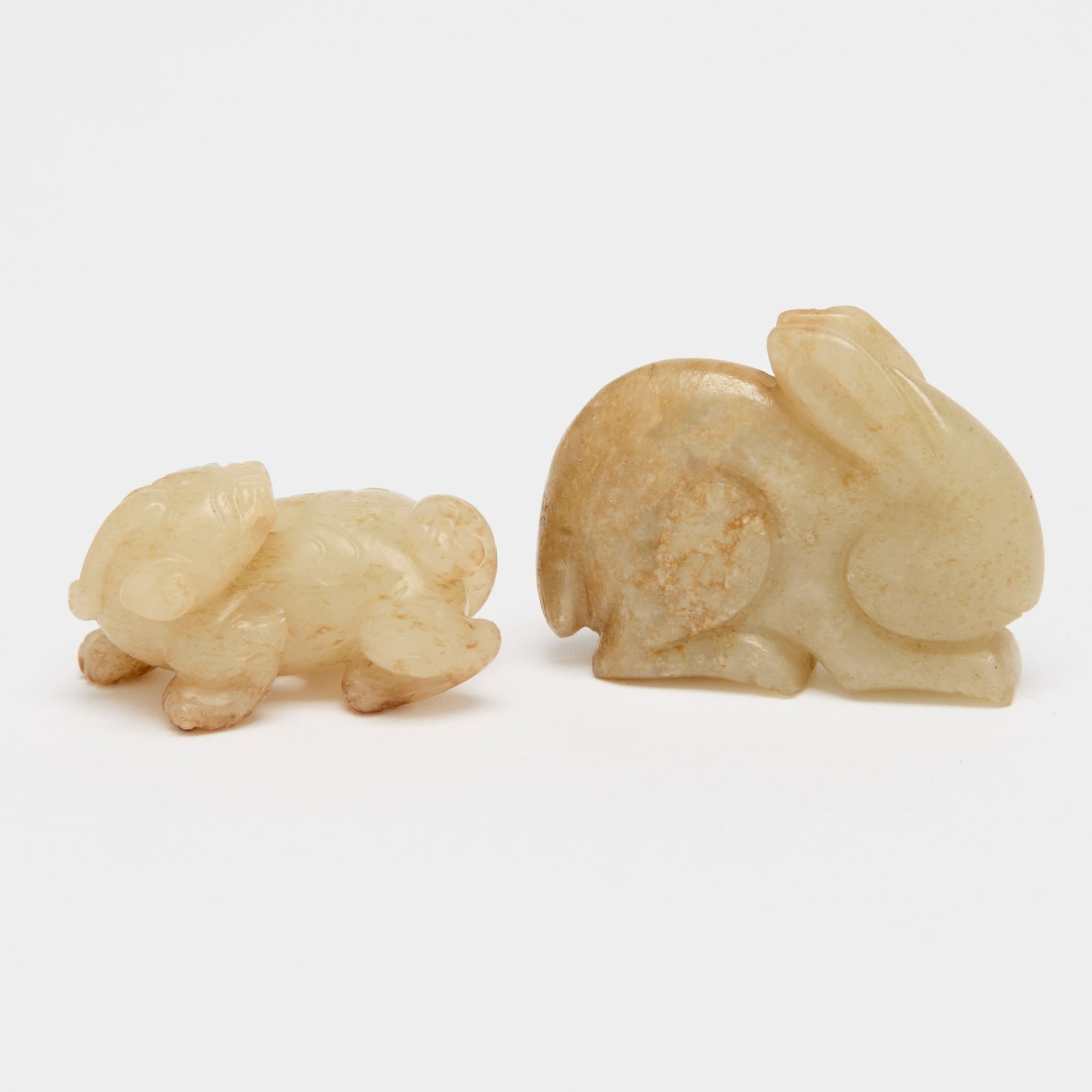 Two Chinese Jade Figural Carvings Ming Dynasty or earlier: Comprising a flattened recumbent rabbit, and a crouching qilin with its head turned and an aperture on its back. (Length of largest 1 1/2 inches)