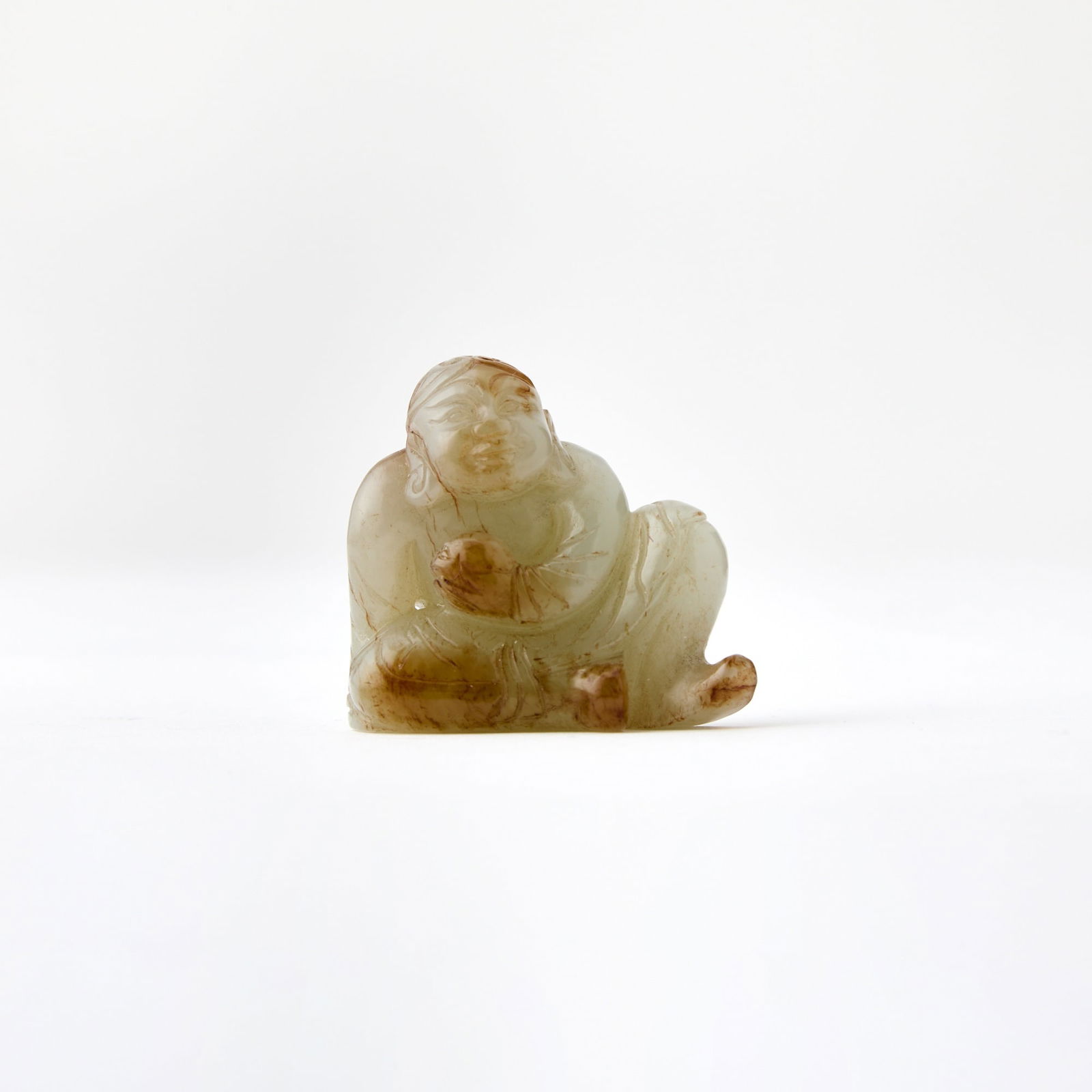 A Chinese Celadon Jade Carving of Liu Hai Early Qing Dynasty: Carved as a half-reclining figure holding a toad, the stone with russet coloring. (Height 1 3/4 inches)