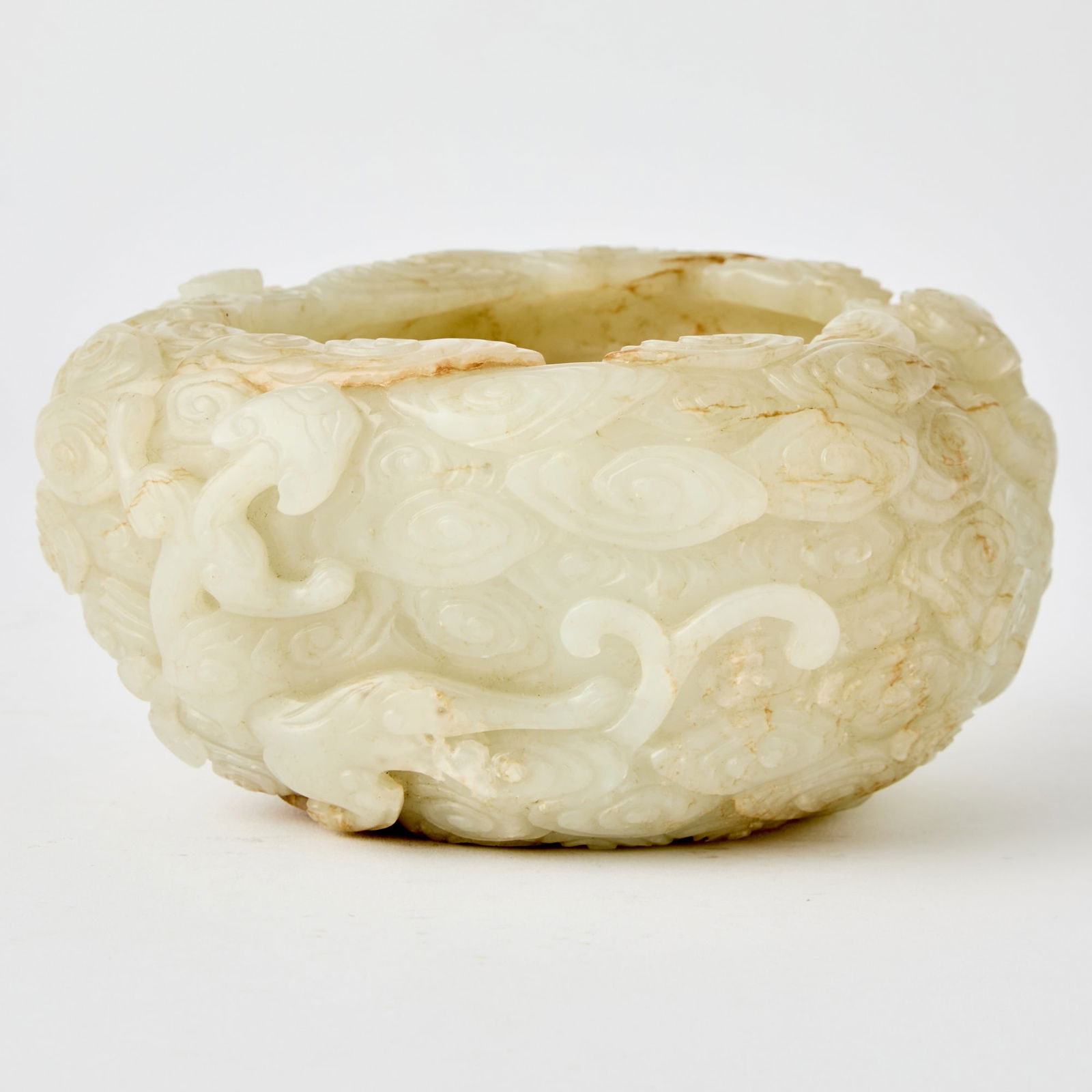 A Chinese Carved Celadon Jade Brush Washer: Of pebble form, the exterior carved in high relief with sinuous chilong writhing amid scrolling cloud motifs. (Length 5 1/2 inches)