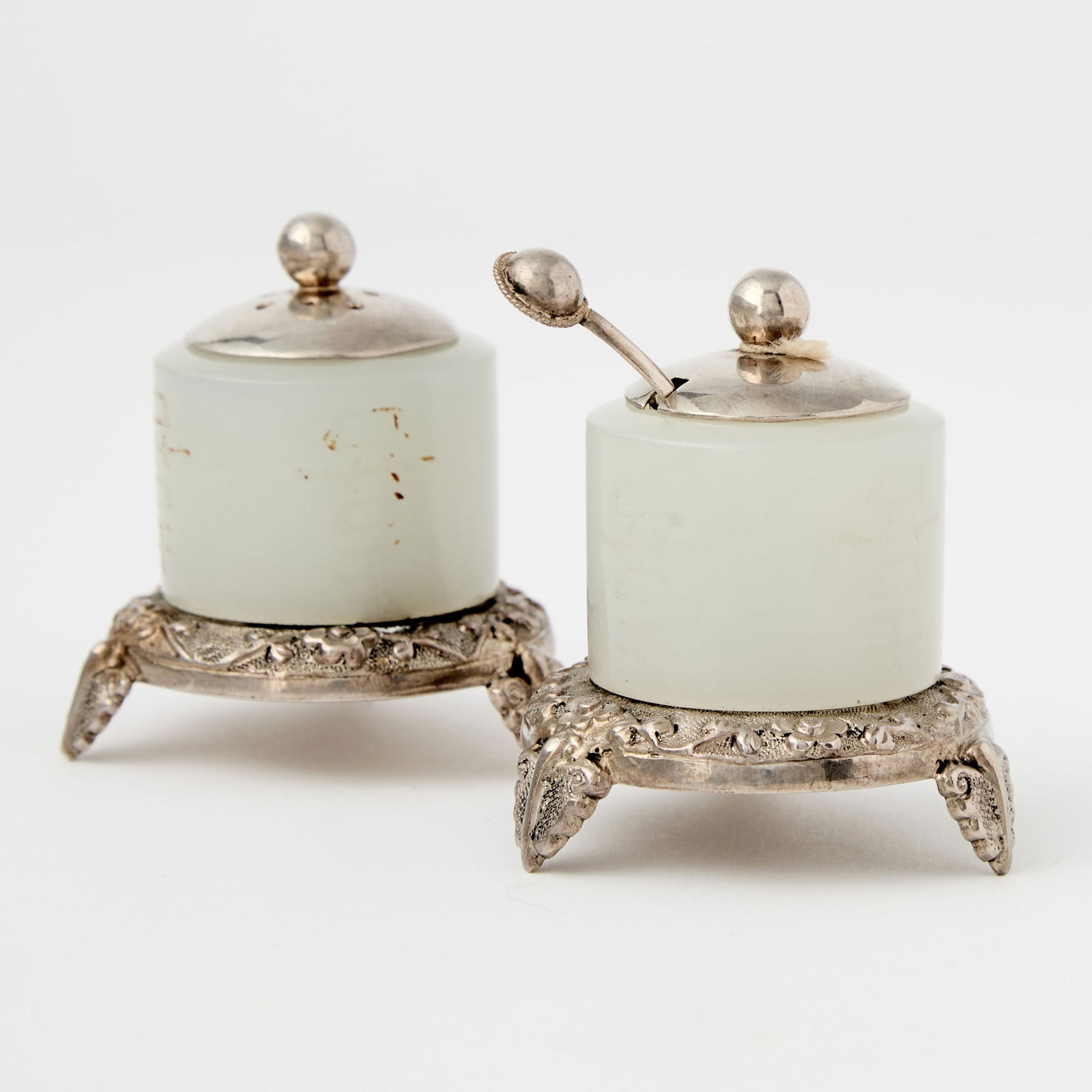A Pair of Chinese Silver-Mounted White Jade Archer Rings 18th Century: Each of cylindrical form, the jade mounted on a silver tripod stand, fitted with silver liner and a cover, the exterior jade carved with ‘xi’ characters. (Diameter of jade 1 1/4 inches)