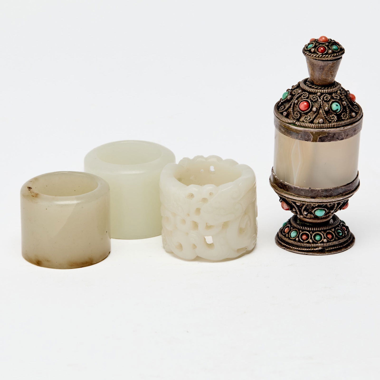 A Group of Chinese Jade and Agate Thumb Rings 19th Century: Comprising one openwork, two unadorned, and one silver-mounted example. (Height of tallest 2 3/4 inches)
