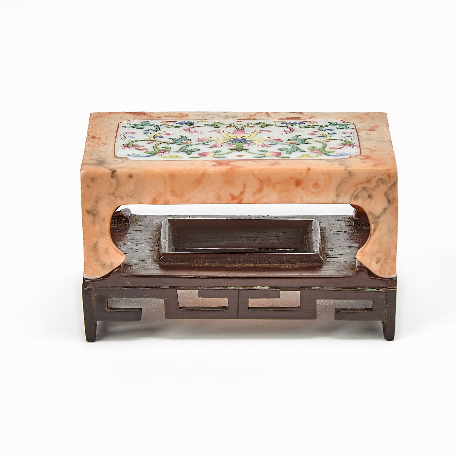 A Chinese Famille Rose Porcelain Inkstone Holder Qing Dynasty: The diminutive bed-form porcelain raised on four thick legs terminating in hoof feet, the top enameled with a central lotus blossom radiating leafy and floral tendrils; with a fitted hardwood stand. (