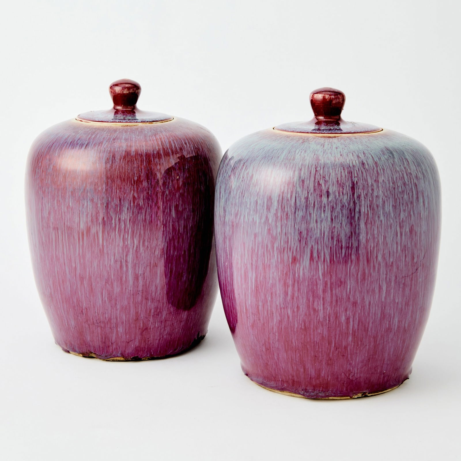 A Pair of Chinese Flambe Glazed Porcelain Jars and Covers 19th century: Each of ovoid form with a domed cover surmounted by a knop, covered overall in a streaked glaze of deep raspberry tones thinning to lavender hues. (Height 9 1/2 inches)