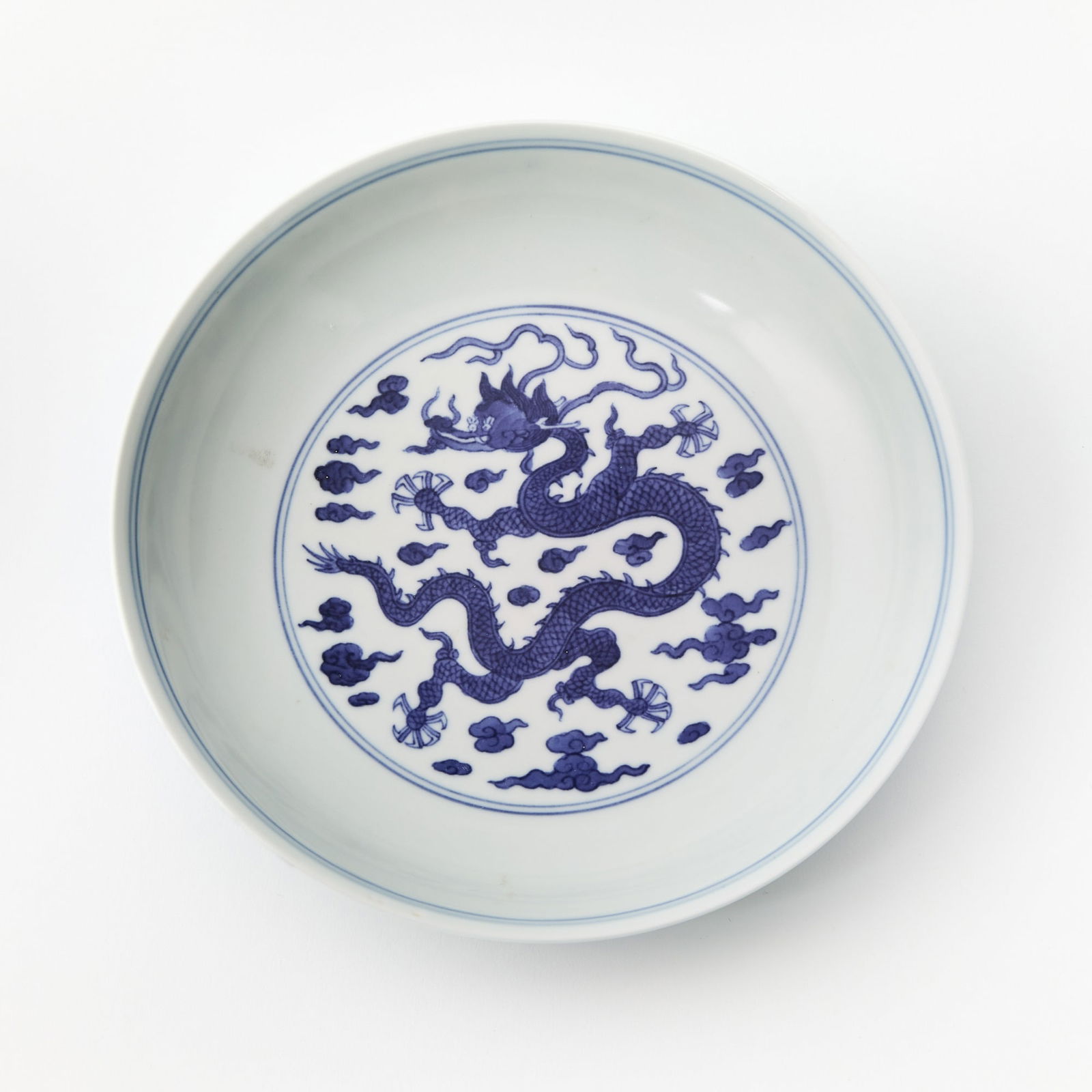 A Chinese Blue and White Porcelain Dish Zhiyuan Tang Mark, 20th century: Decorated with a central roundel featuring a scaly dragon writhing among cloud scrolls, the exterior adorned with a similar design. (Diameter 6 3/4 inches)